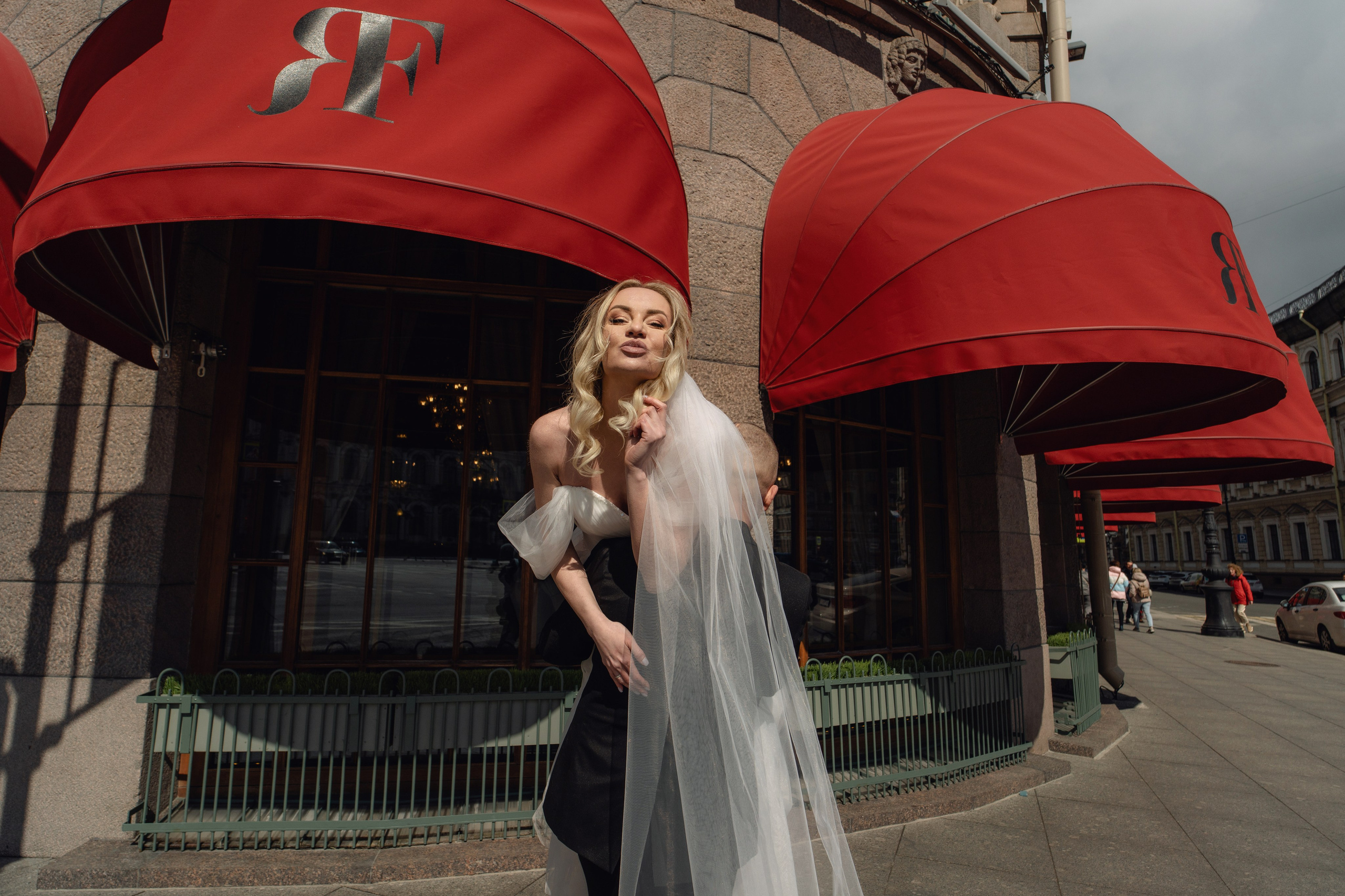 жених несет невесту под красными маркизами гостиницы Астория. Свадебная фотосессия у Астории.