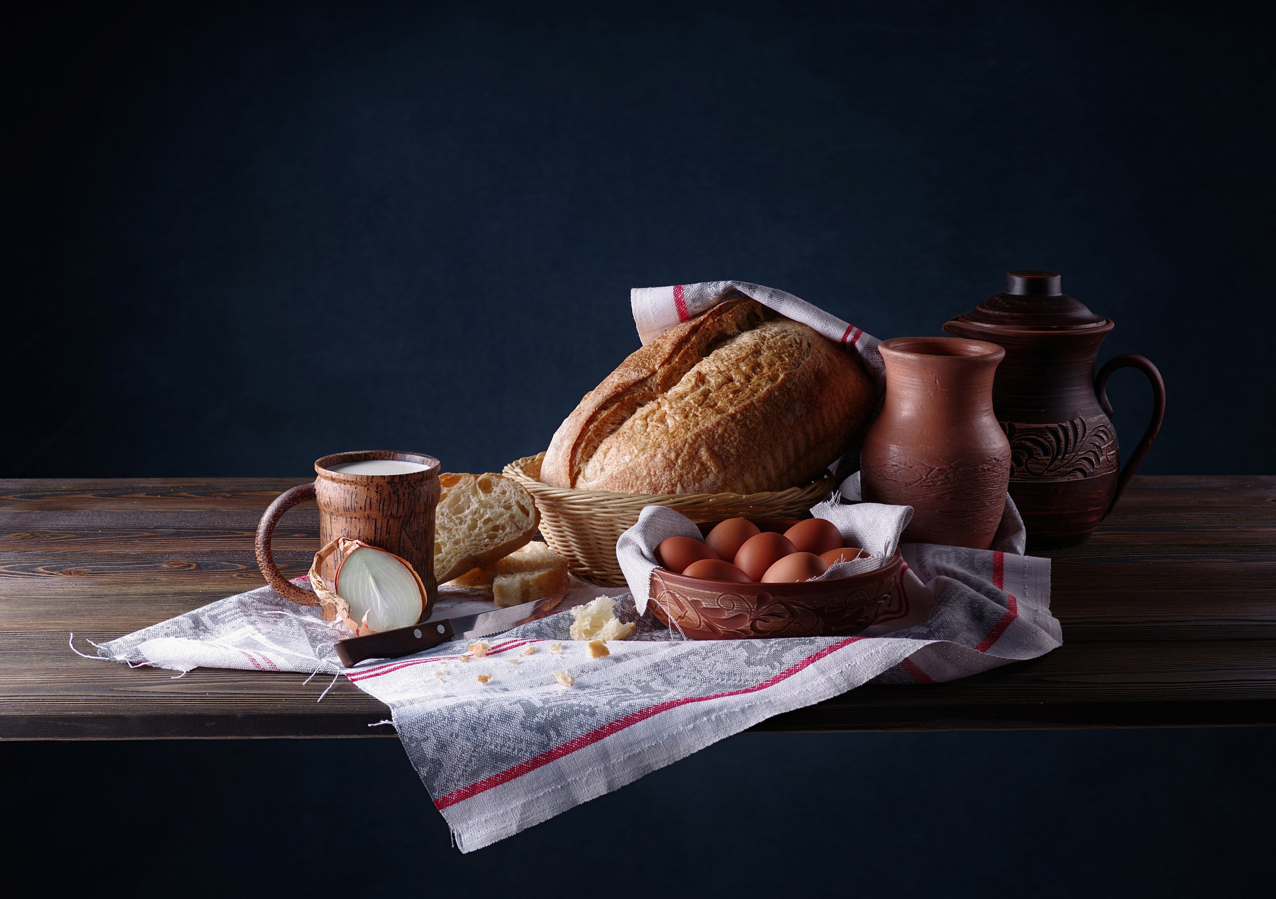 Натюрморт их хлеба, кувшинов, яиц в  глиняной чаше, кружки с молоком, на тканной салфетке, на деревянном столе 