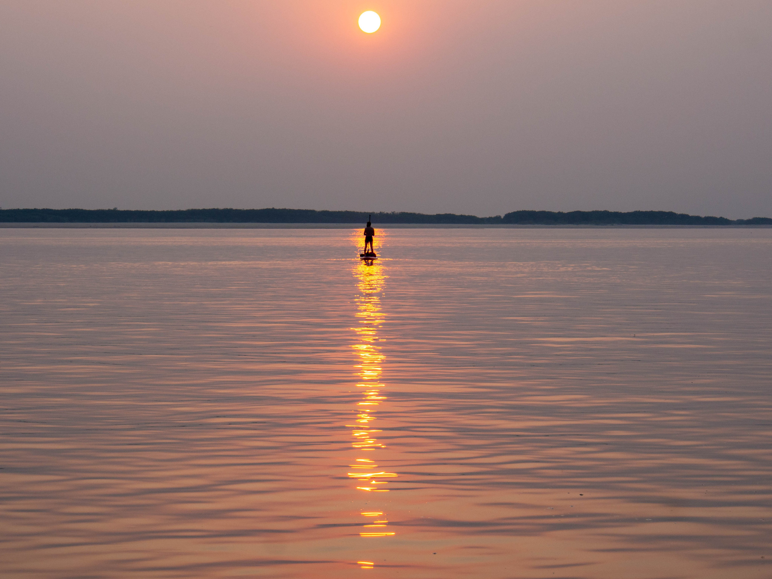 человек на сап-борде на солнечной дорожке, закат