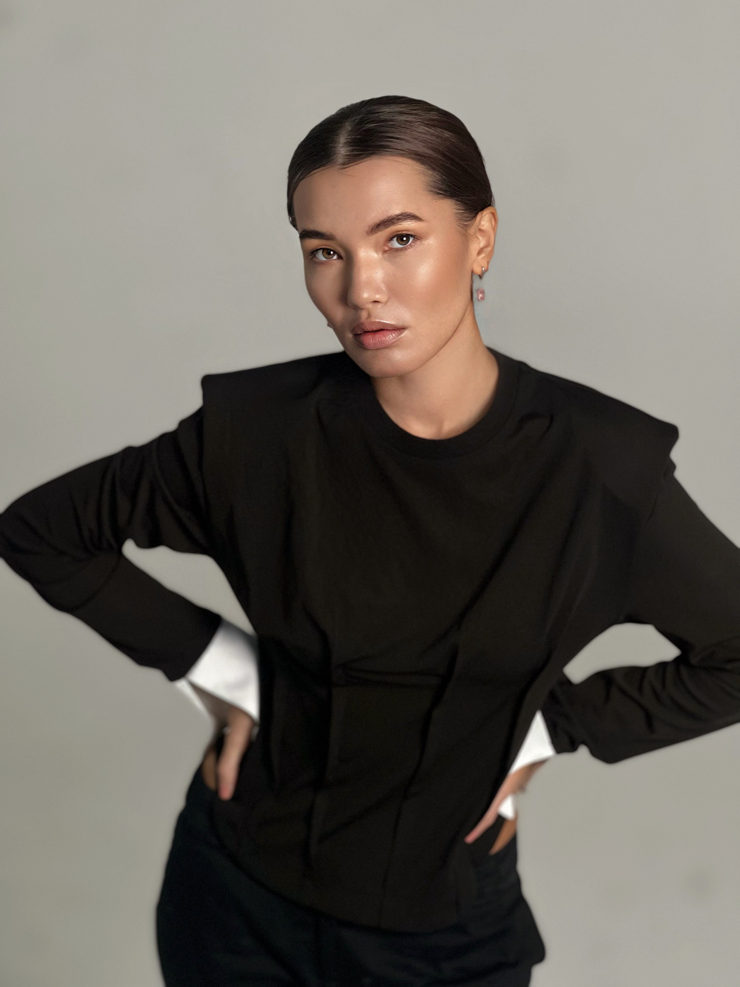 Девушка азиатской внешности позирует в черной одежде на сером фоне