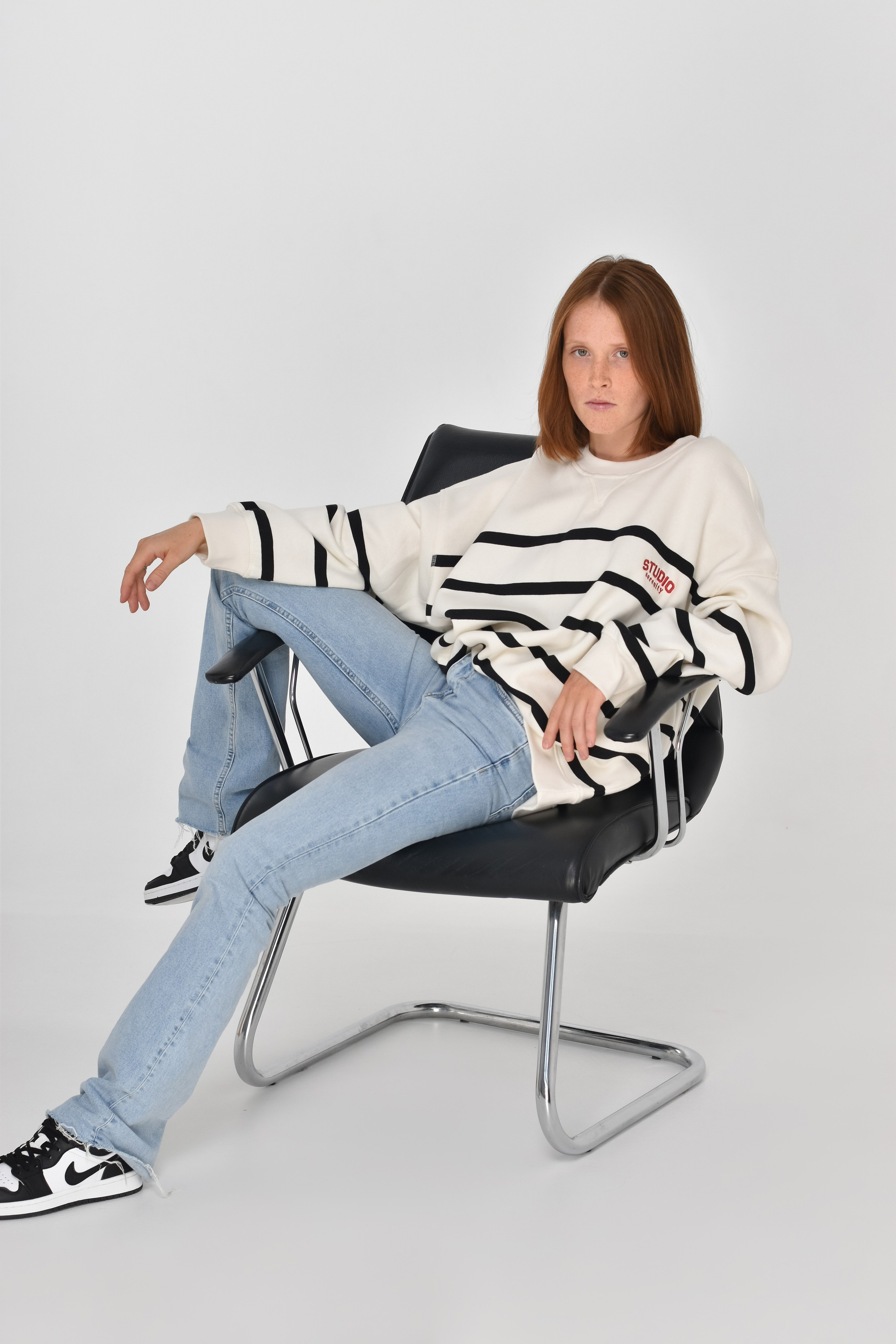 Рыжая девушка модель сидит на стуле в кофте и голубых джинсах