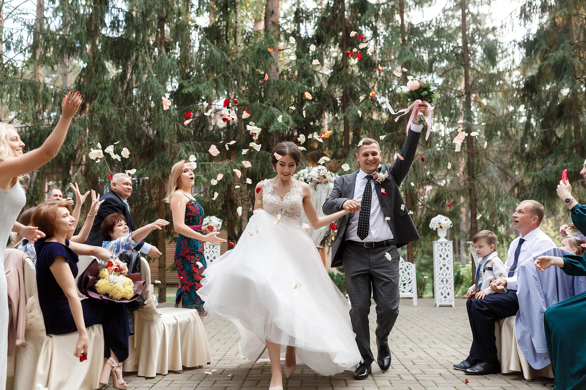 Счастливые жених и невеста бегут по по дорожке мимо гостей