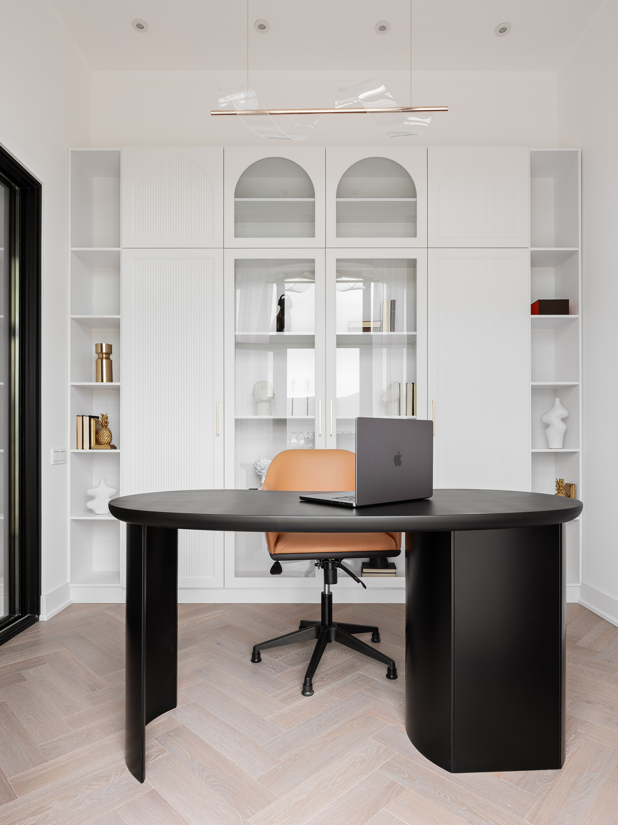 Интерьер домашнего офиса в современном стиле: минималистичный чёрный стол, мягкое эргономичное кресло, встроенные шкафы с витринами и белыми полками для декора. Автор проекта — дизайнер Василисса Бачева, стилист Наталья Якушева, фотограф Сергей Денисенко.