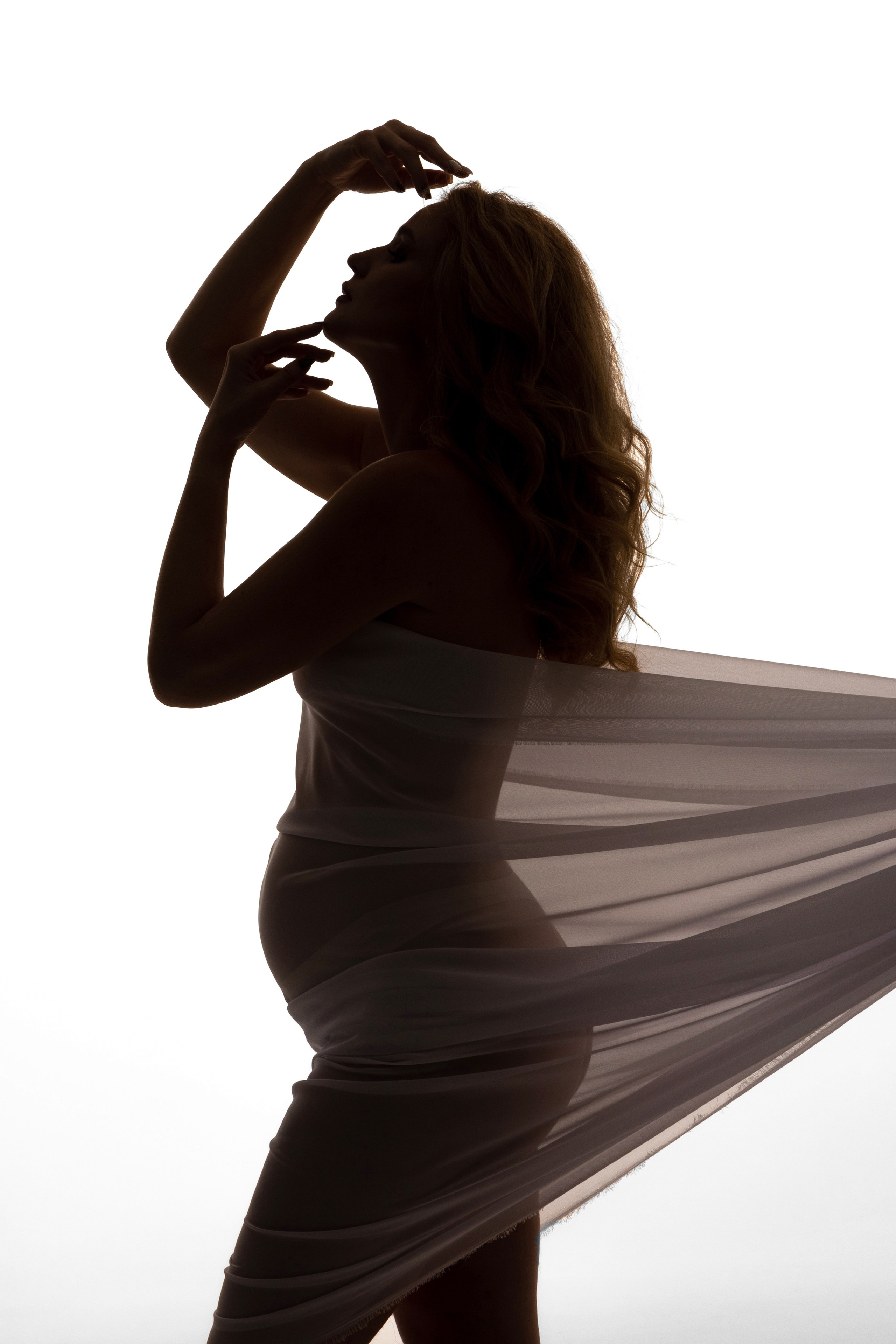 Силуэт стоящей беременной девушки в тканях, держит руки ко лбу