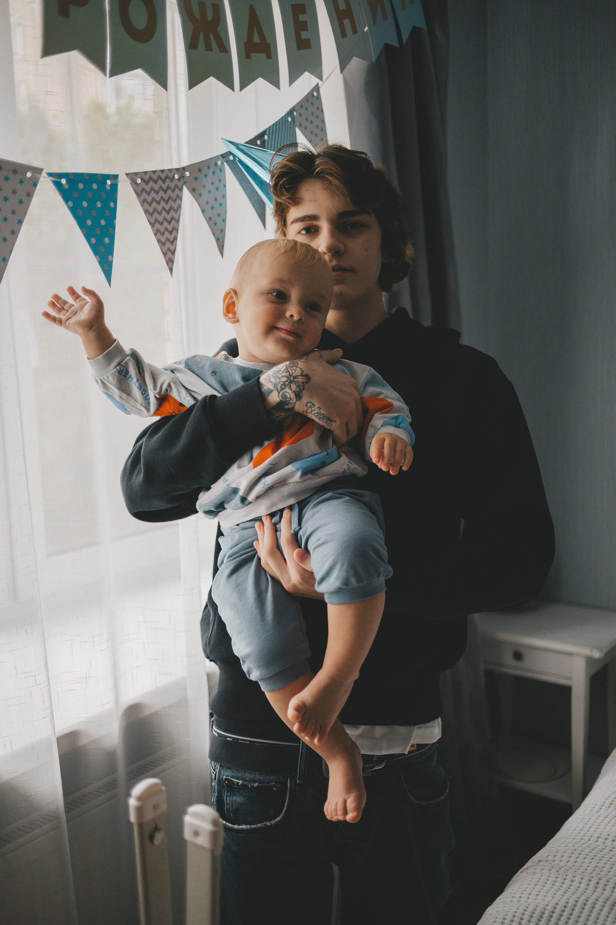 младший брат на руках у старшего, на голове колпачок 