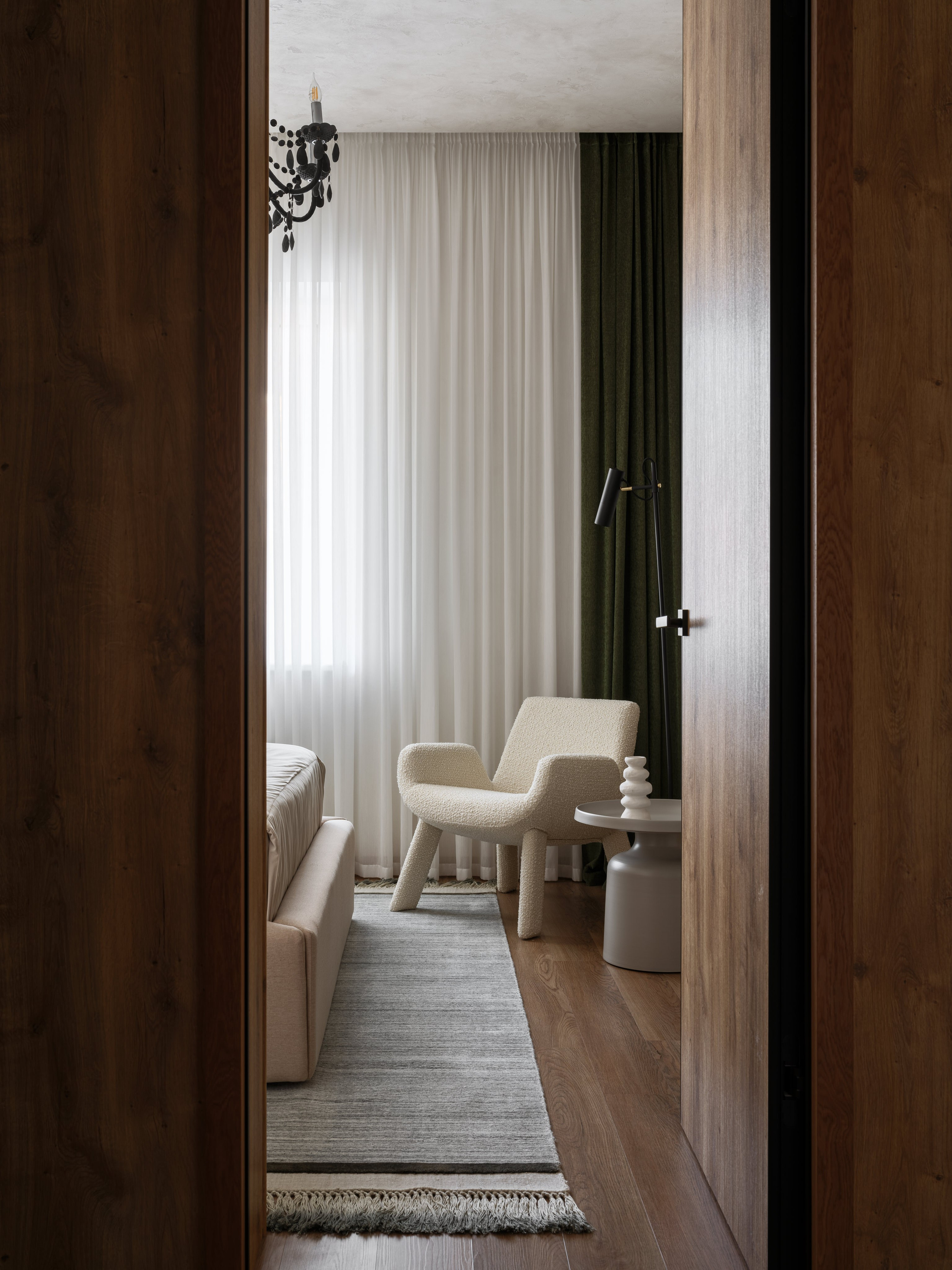 Вид на спальню с современным белым креслом, светло-серыми шторами и зелёными акцентами. Интерьер оформлен Наталией Шелепниковой, фотография Сергея Денисенко, стилизация Алёны Бершацкой.