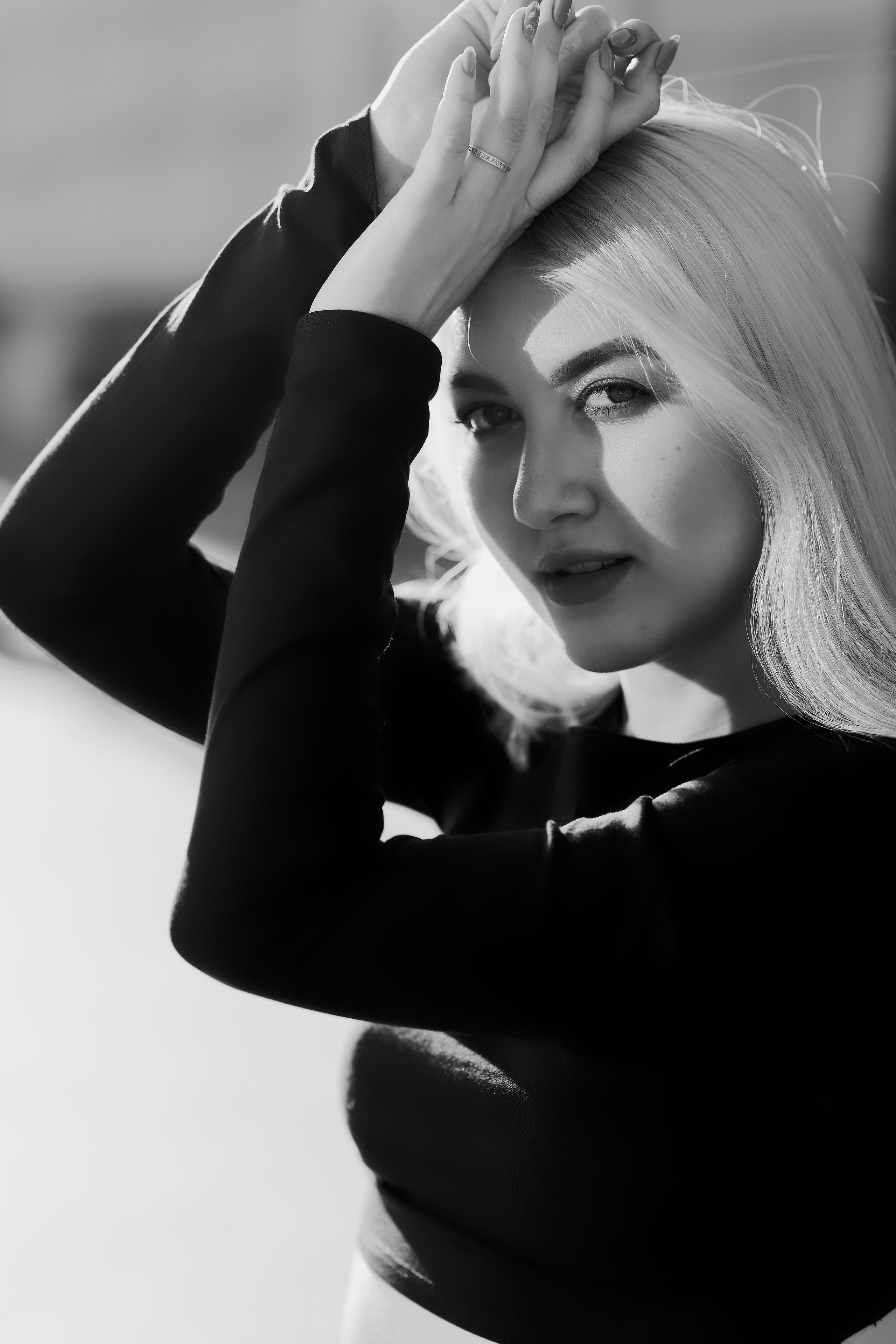 Крупный план портрета в черно-белом исполнении, блондинка с руками над головой, драматичное освещение, чувственный образ