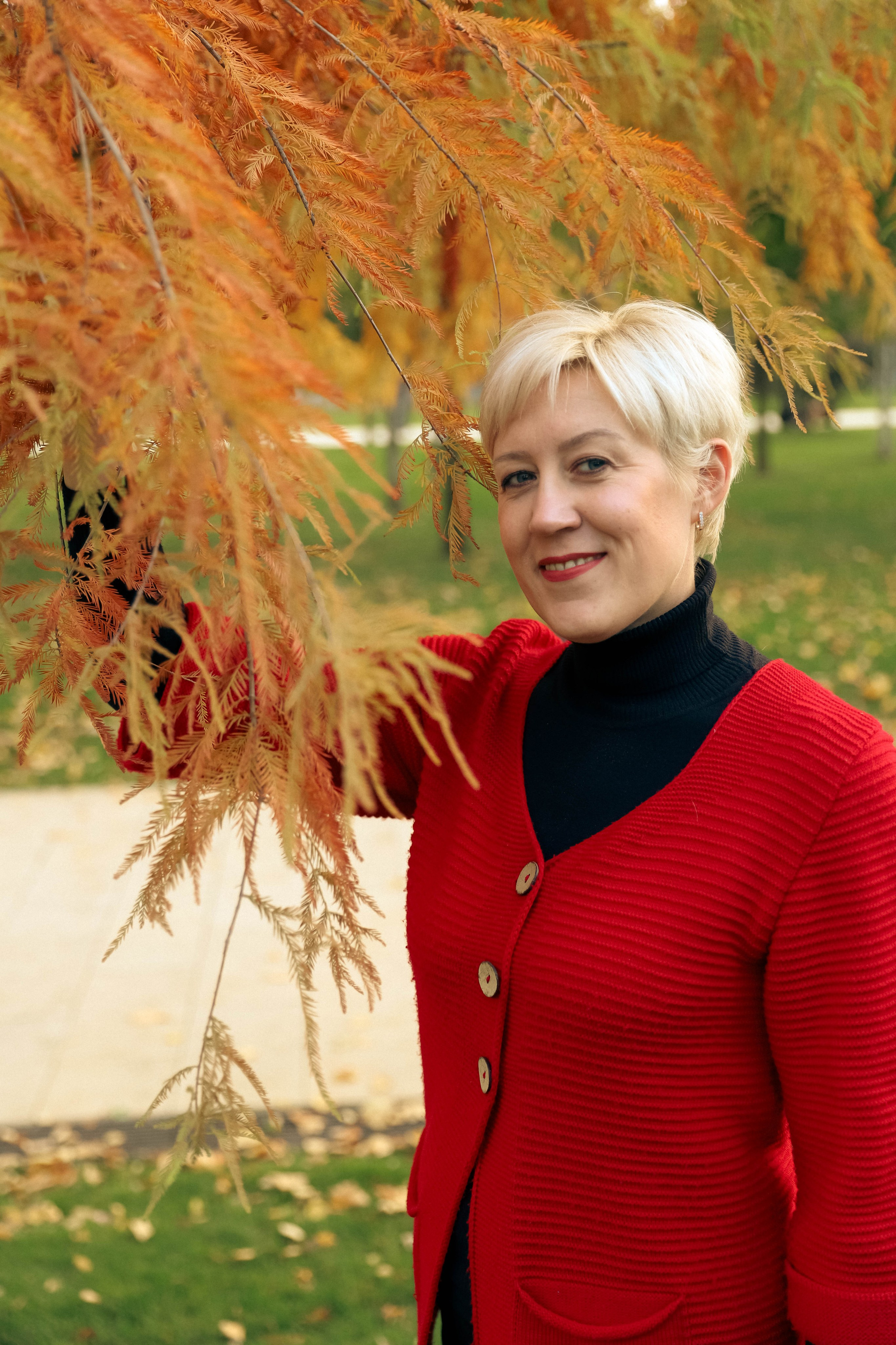 Фотопрогулка по парку: девушка в красном кардигане позирует на фоне ярких осенних деревьев