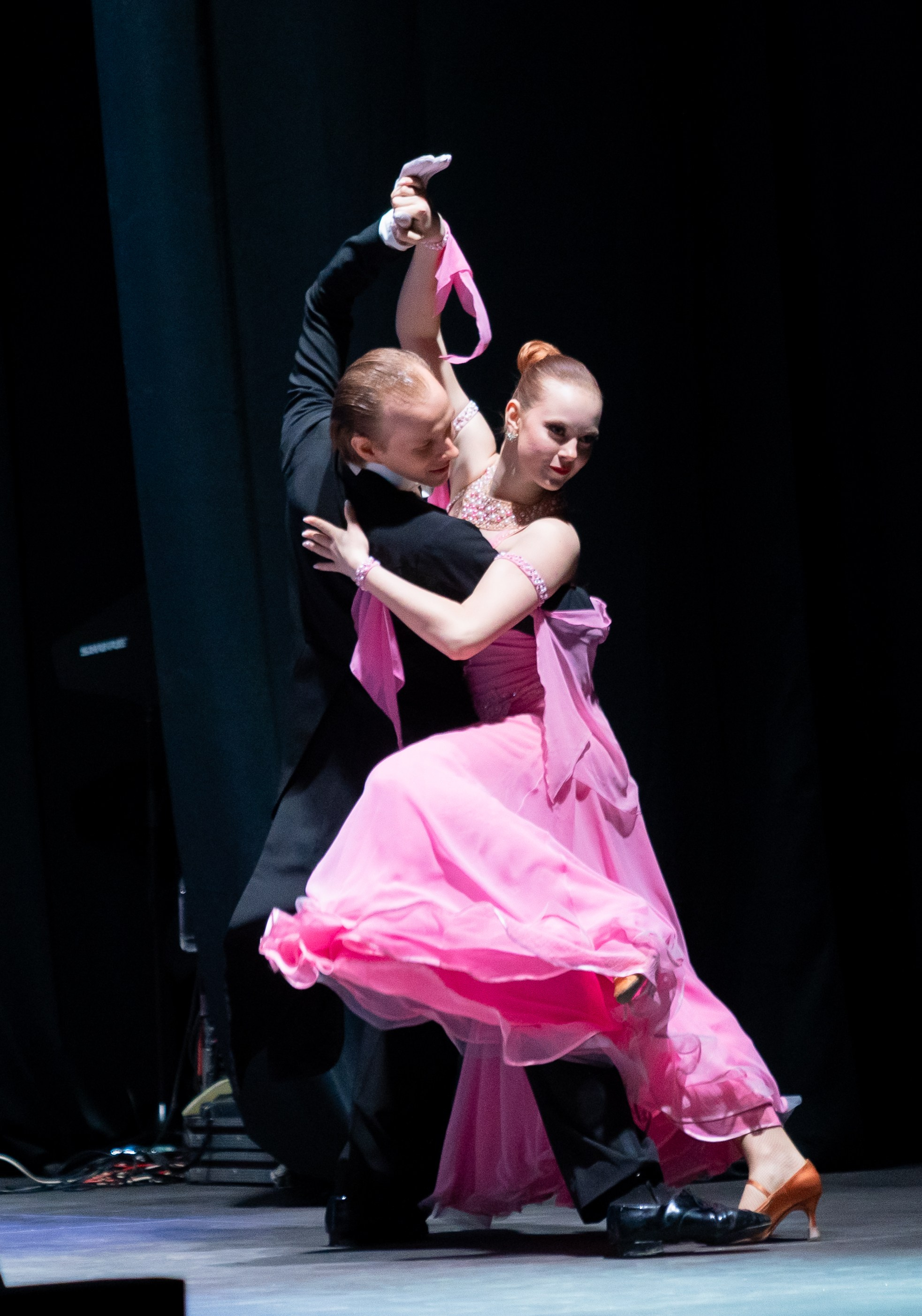 Энергичный бальный танец в розовых тонах. Партнёрша в пышном розовом платье и партнёр в чёрном фраке выполняют сложную поддержку. Концерт ко Дню местного самоуправления. Фото Евгения Мальцева.