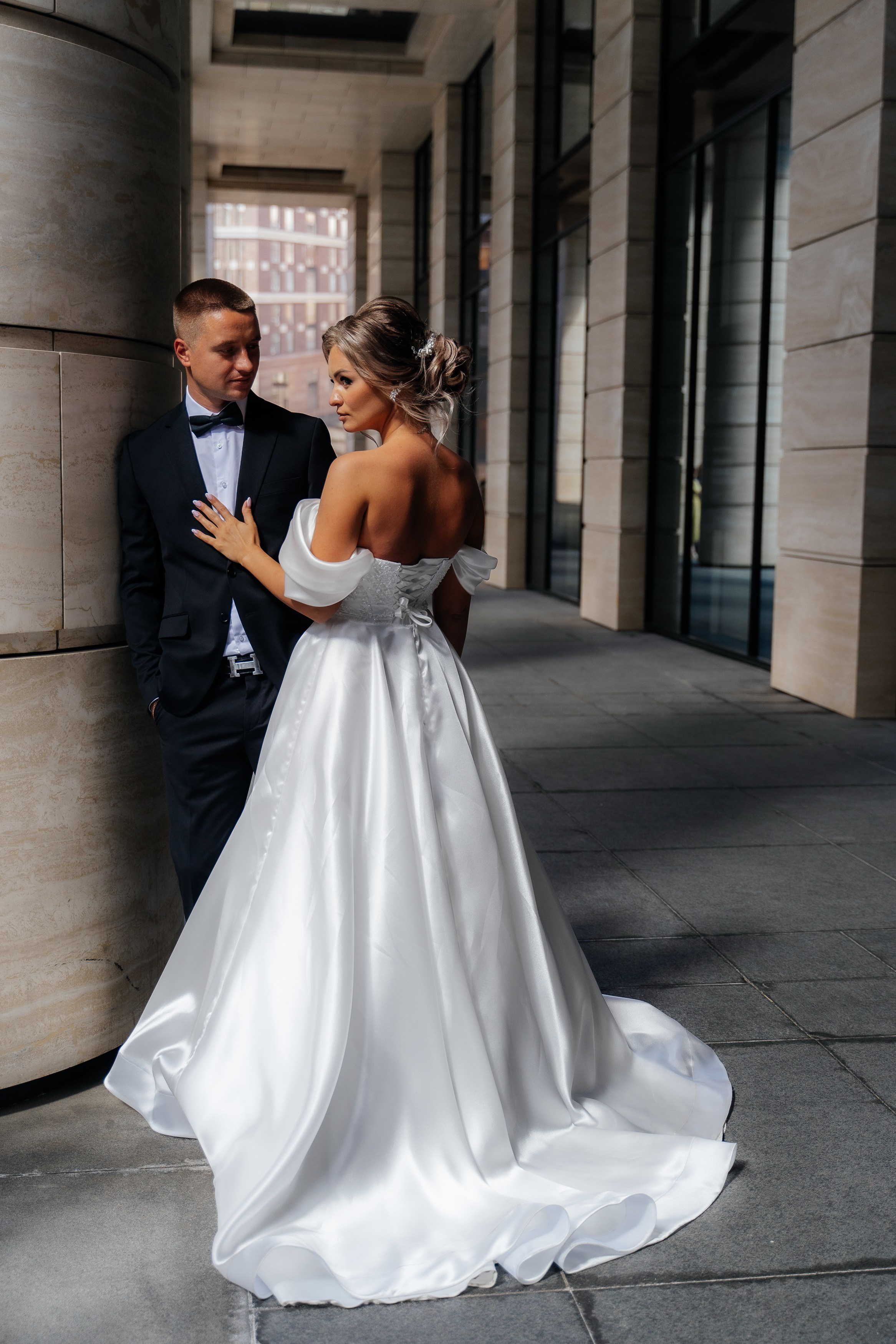 Свадебная фотосессия в Невской ратуше. Стильные жених и невеста стоят рядом у колоны 