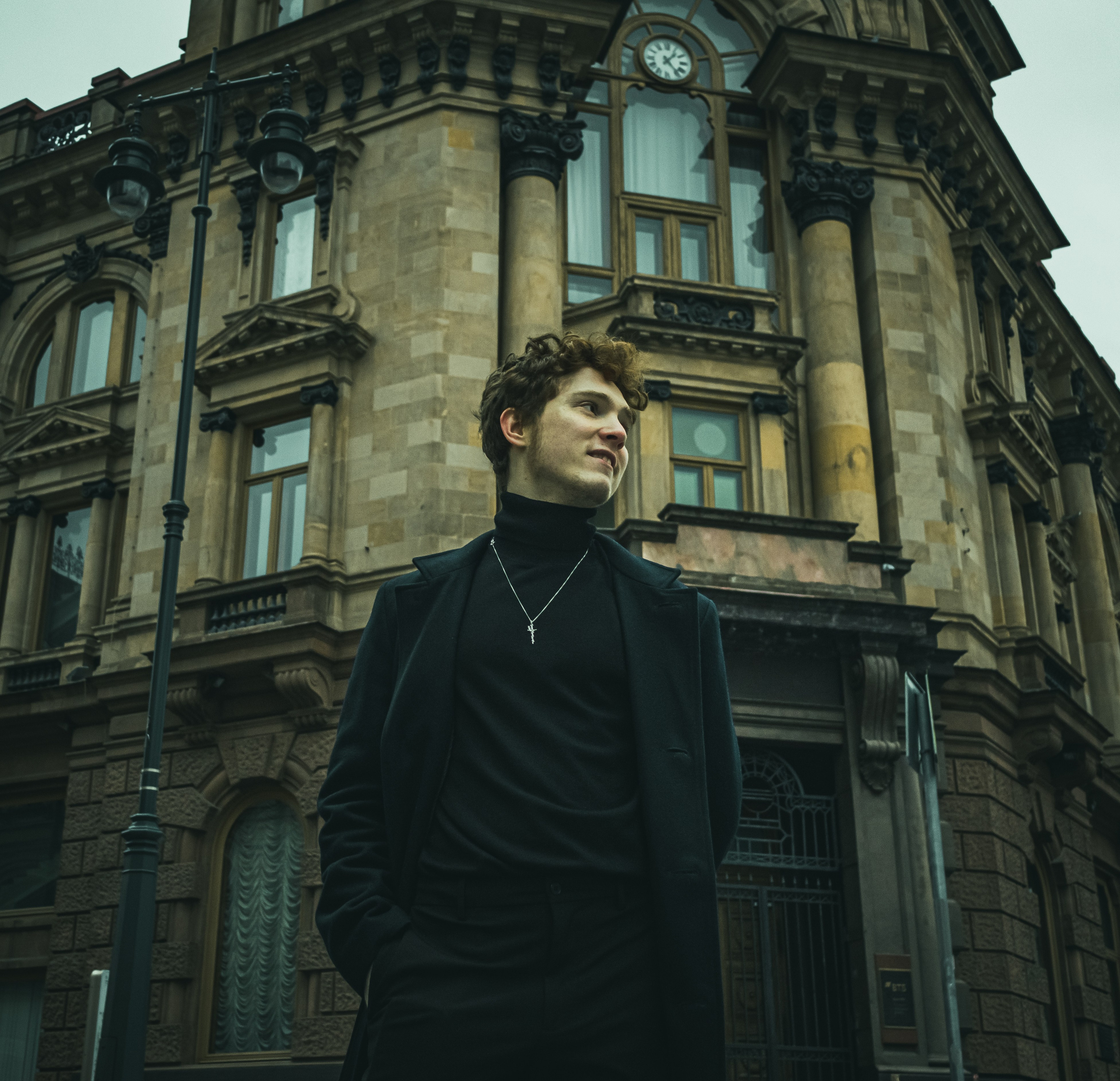 Уличный портрет улыбающегося рыжего парня на фоне здания.