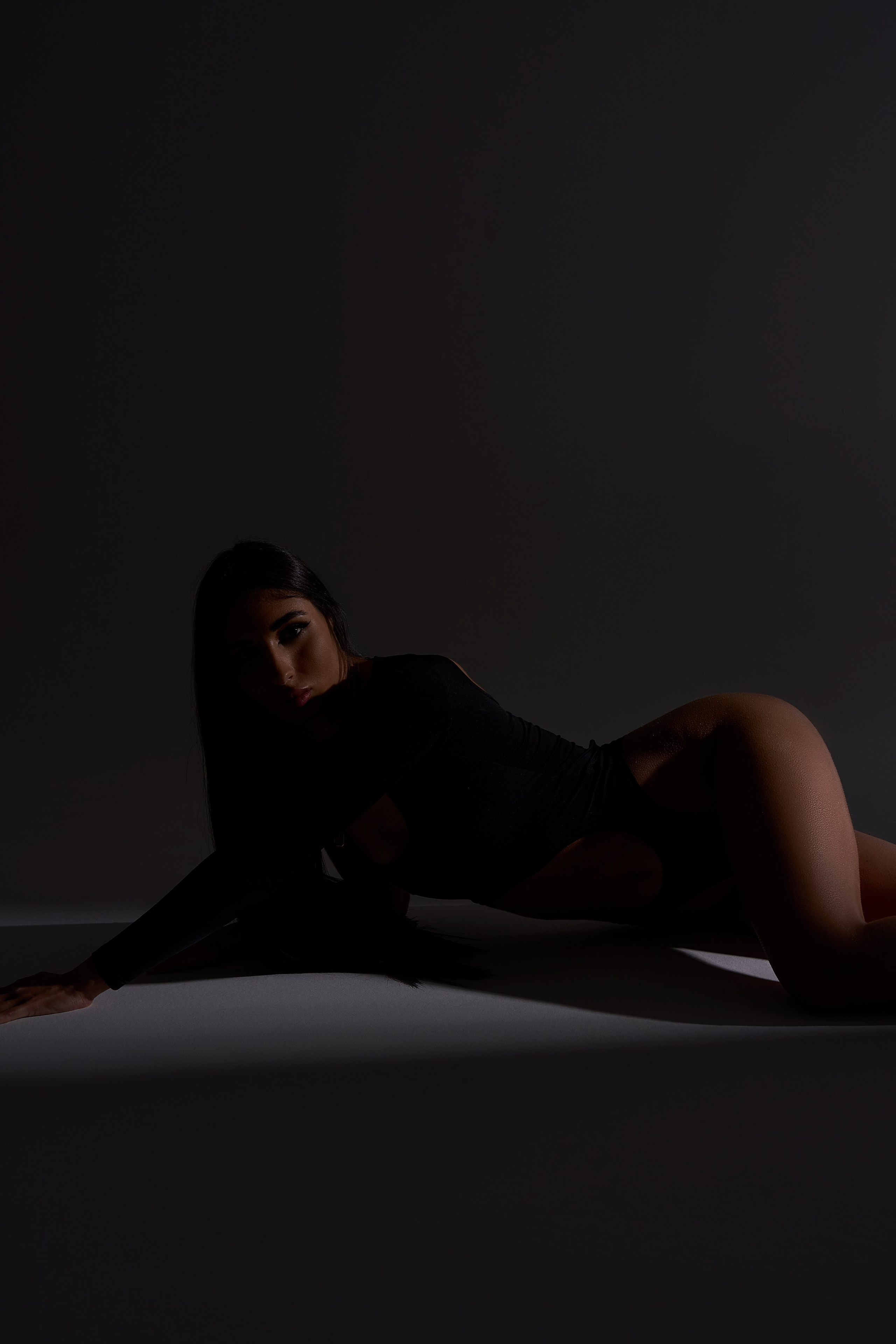 Фотосессия в студии Москвы: девушка в чёрном боди, лежит в тени, нюансная пластика тела, спокойствие кадра