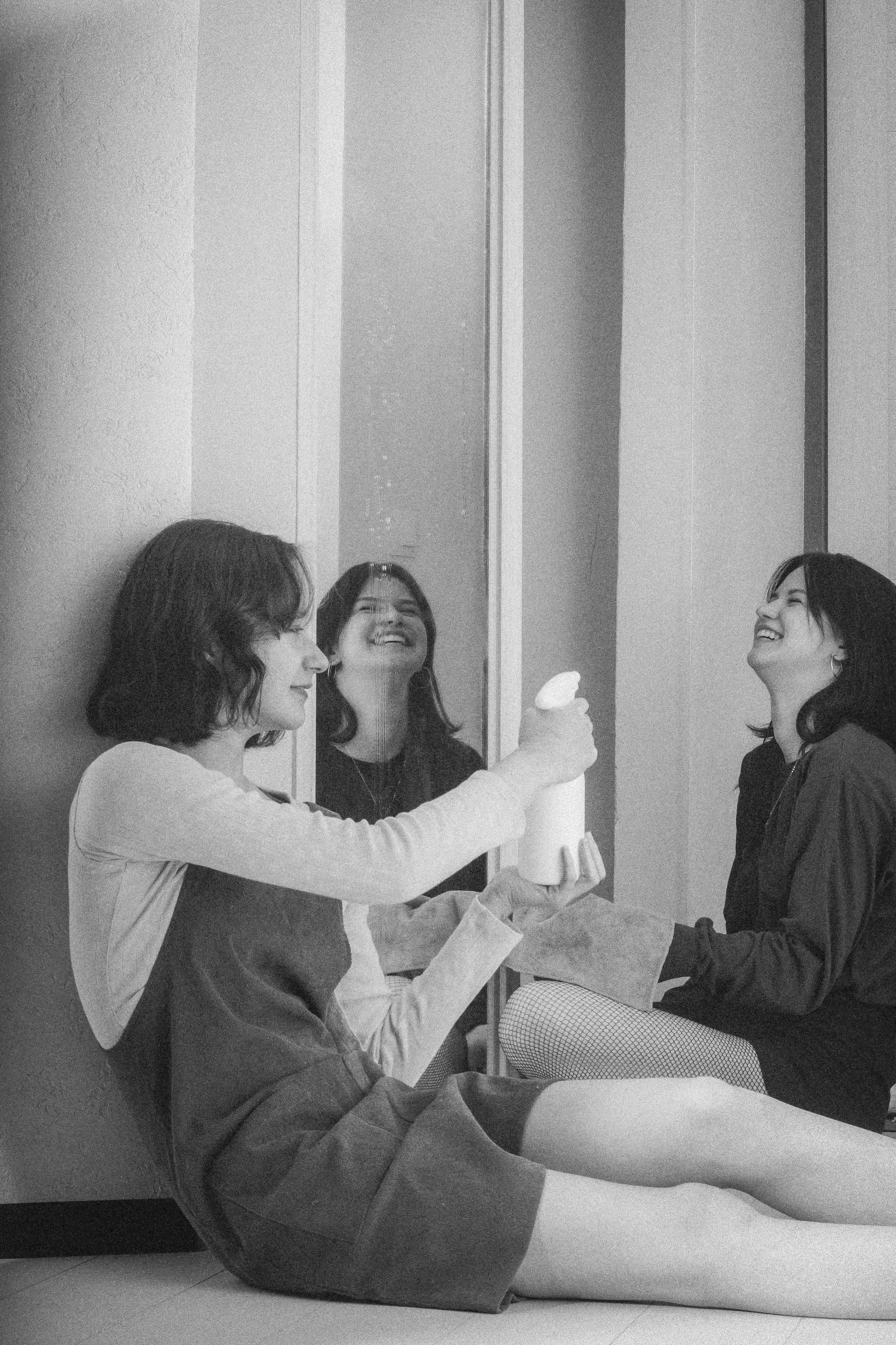 Две девушки смеются у зеркала, распыляя воду — прошлое, которое живёт только в памяти.