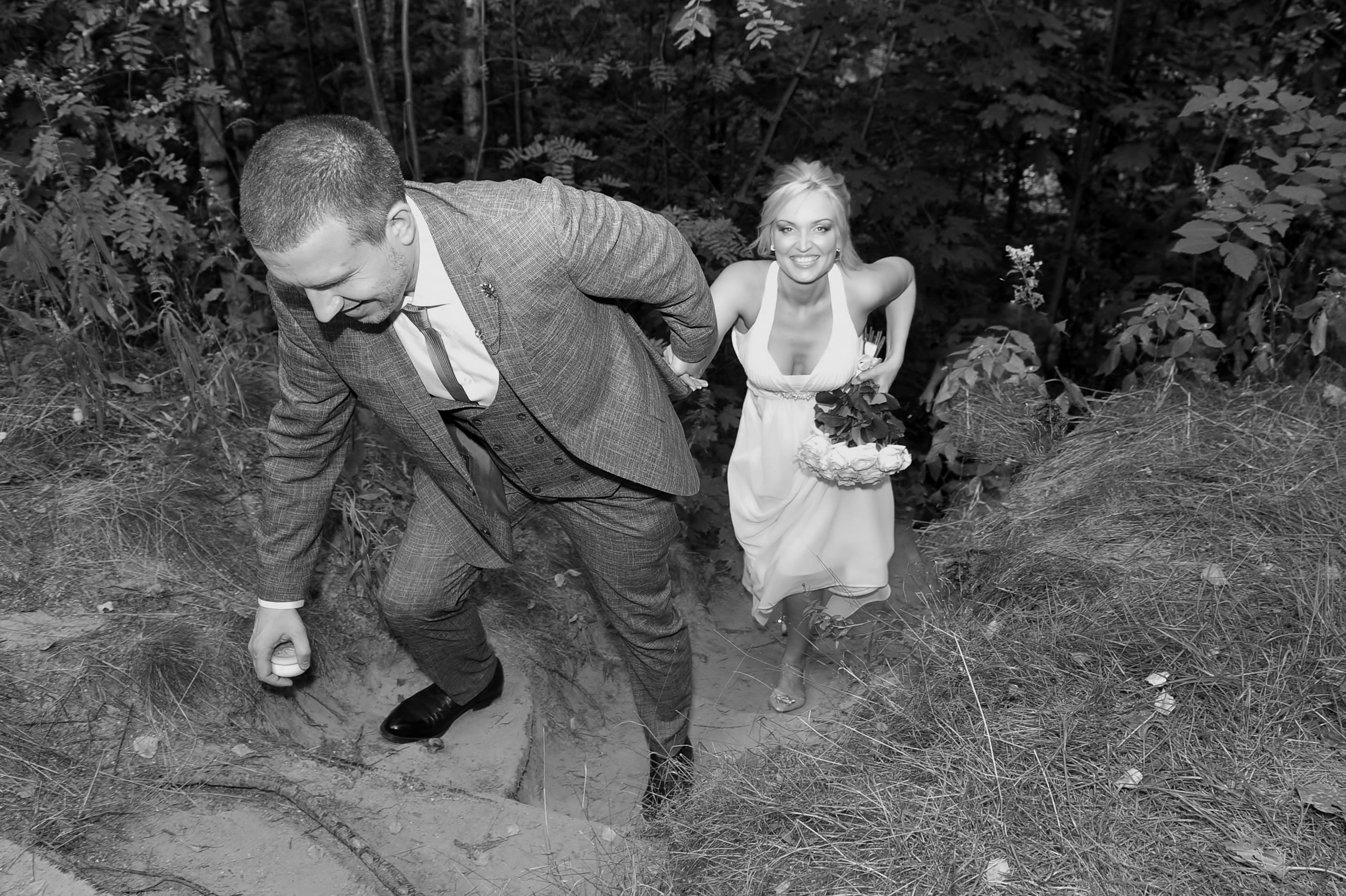 Свадьба на Воробьёвых Горах рядом с МГУ, новобрачные лезут в гору, жених тянет за собой в гору невесту, у жениха в руке просвирка из храма, черно-белая фотография