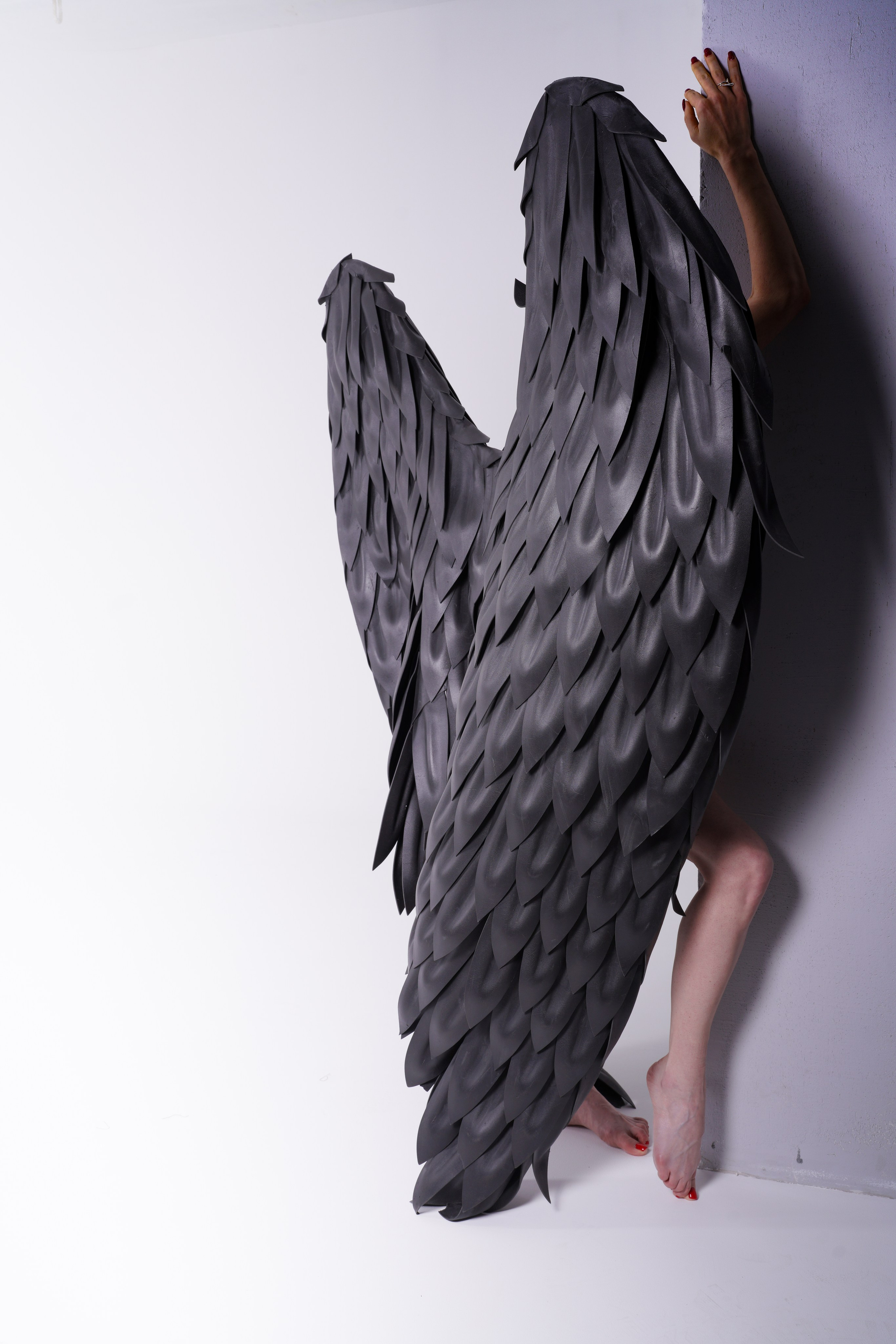 Человек в черных крылья прижимается к стене закрывая крыльями лицо