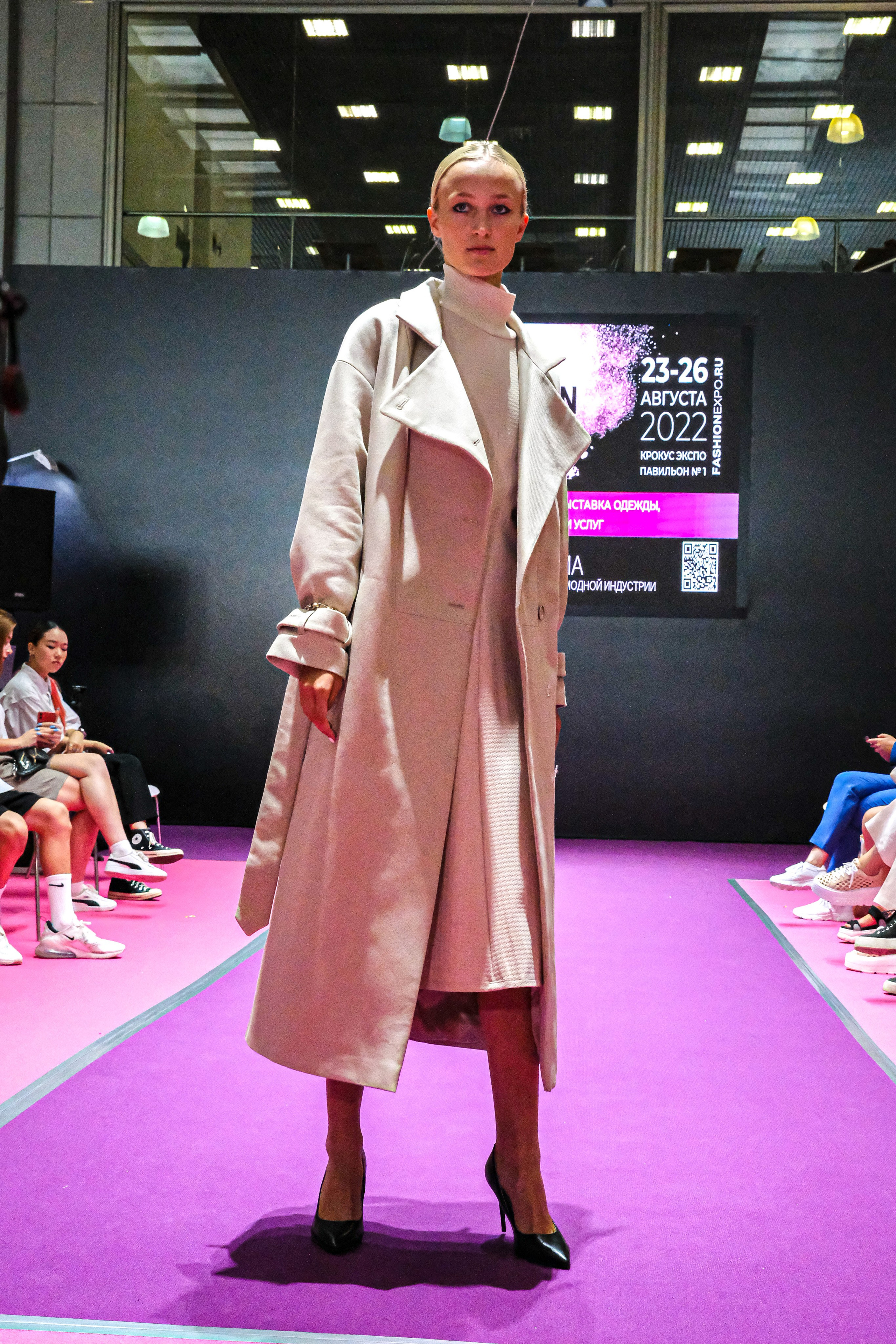  "Модели в ярких нарядах проходят по подиуму во время показа мод, освещенные яркими софитами и окруженные восторженными зрителями."