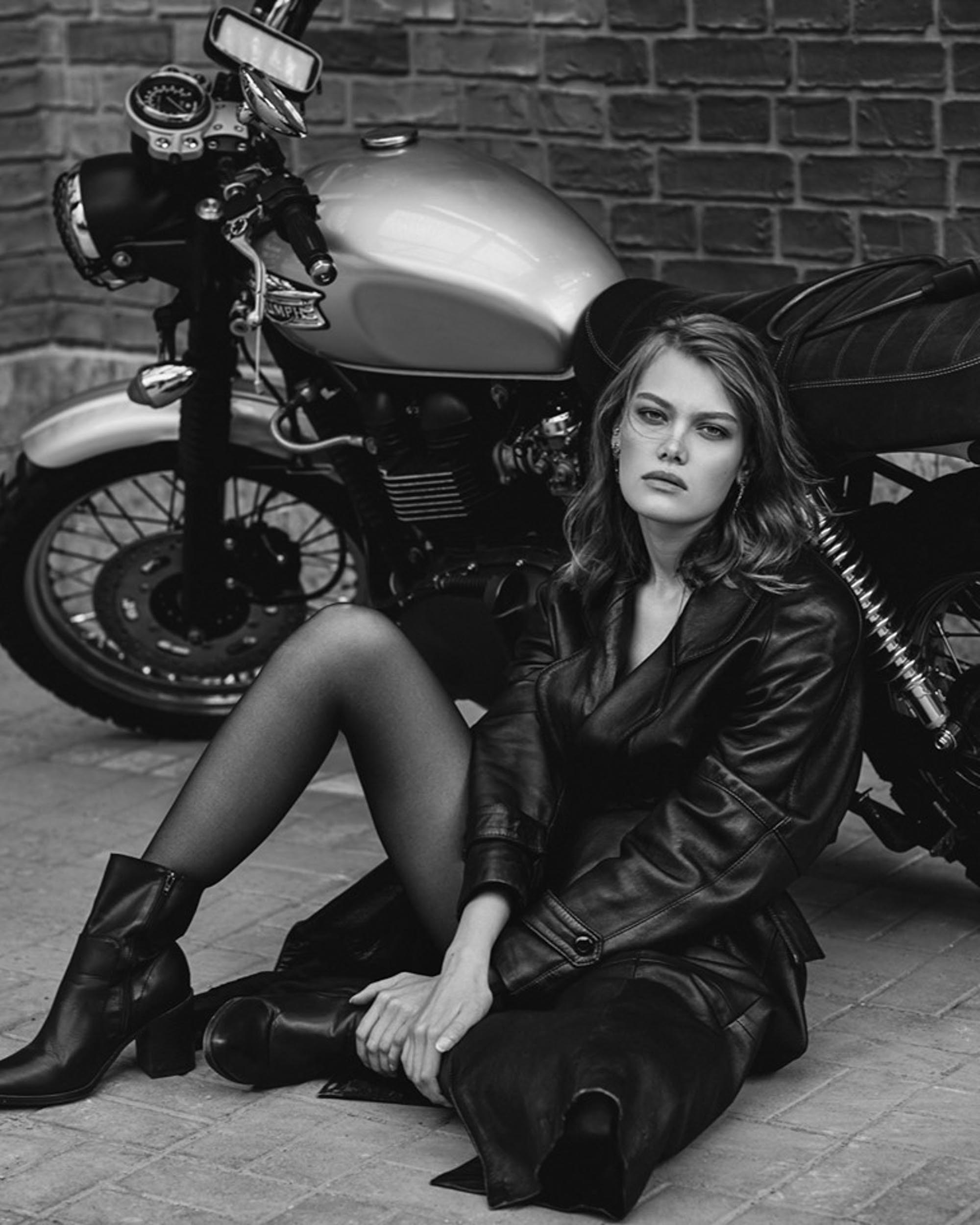 Девушка в кожаной куртке сидит рядом с мотоциклом