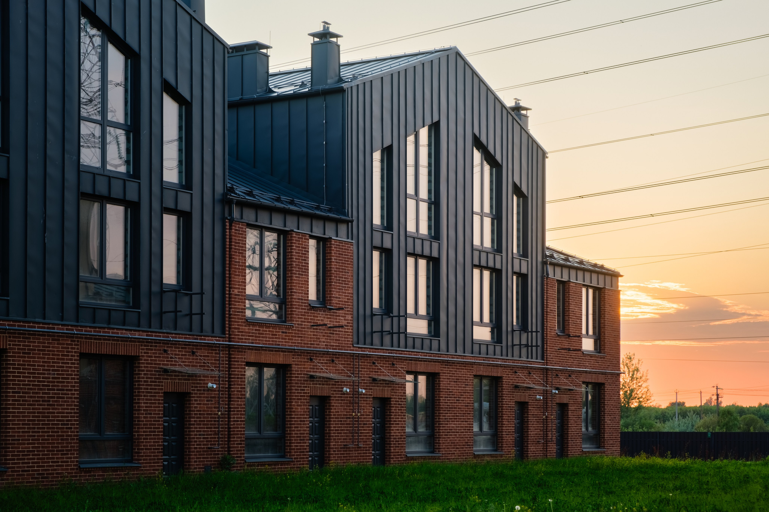 Современный кирпичный коттедж с черными элементами на фасаде. Здание имеет несколько этажей и большие окна.