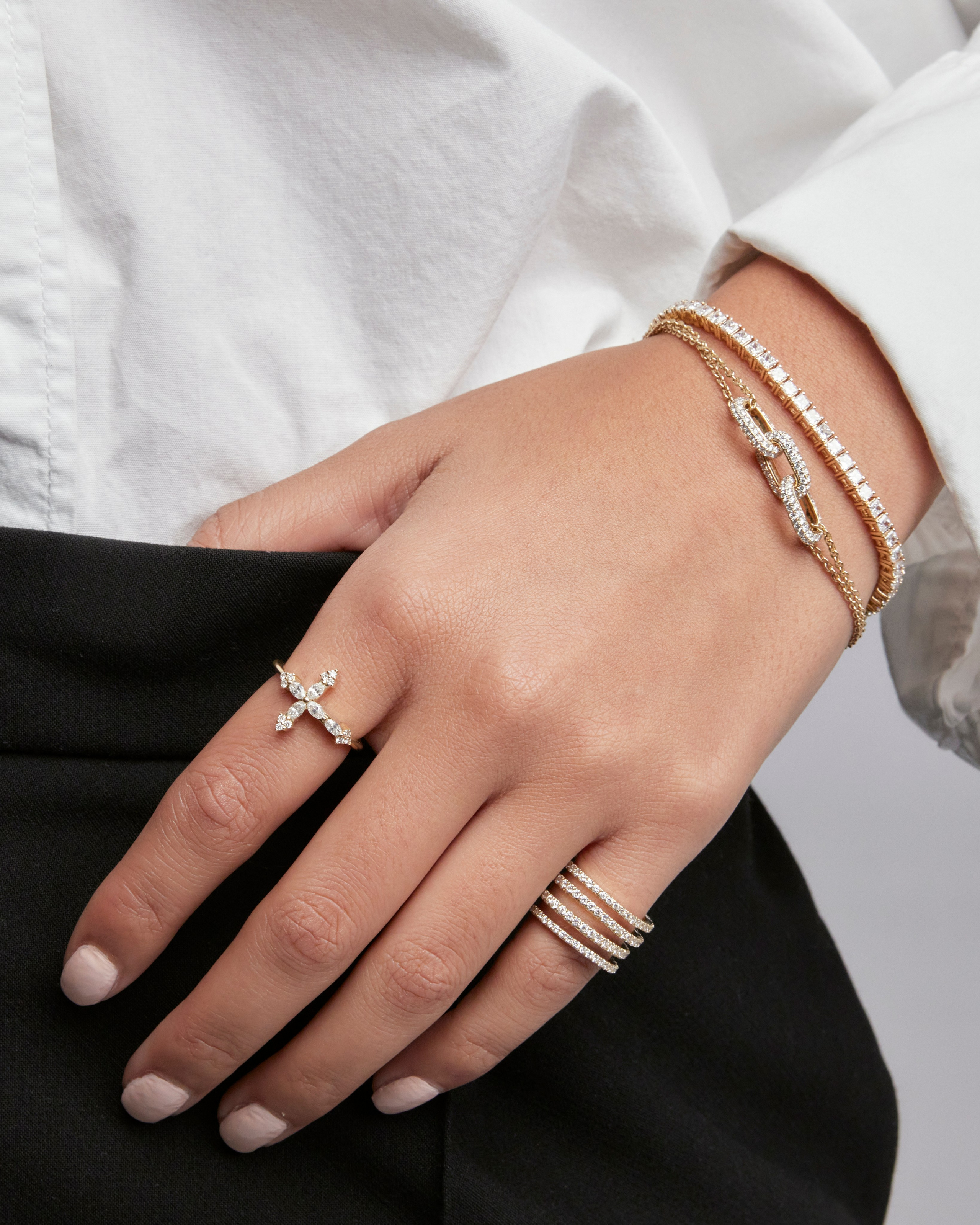 Close-up of a model's hand wearing layered gold bracelets and diamond-encrusted rings, showcasing elegant and modern jewelry design.