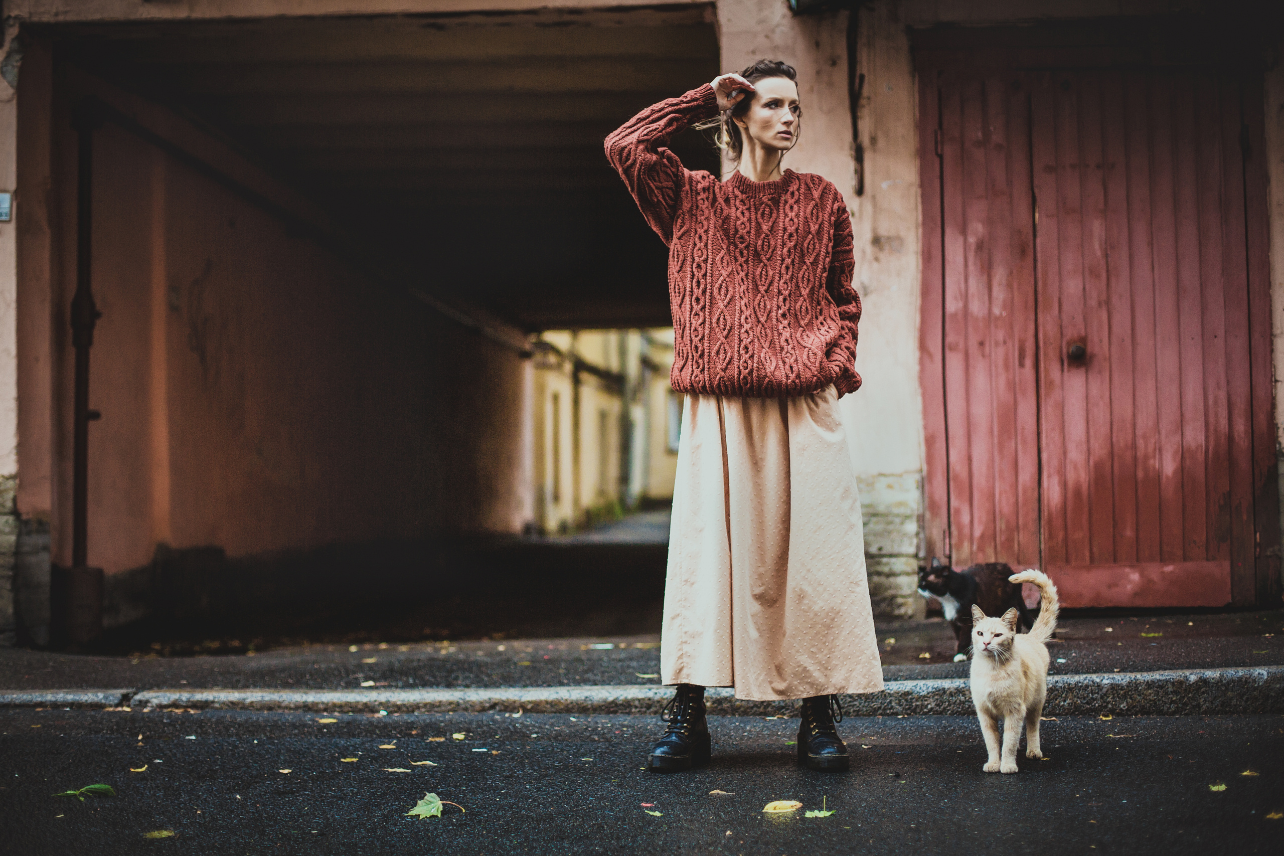 девушка в красном вязаном свитере с котами на улице около красной двери