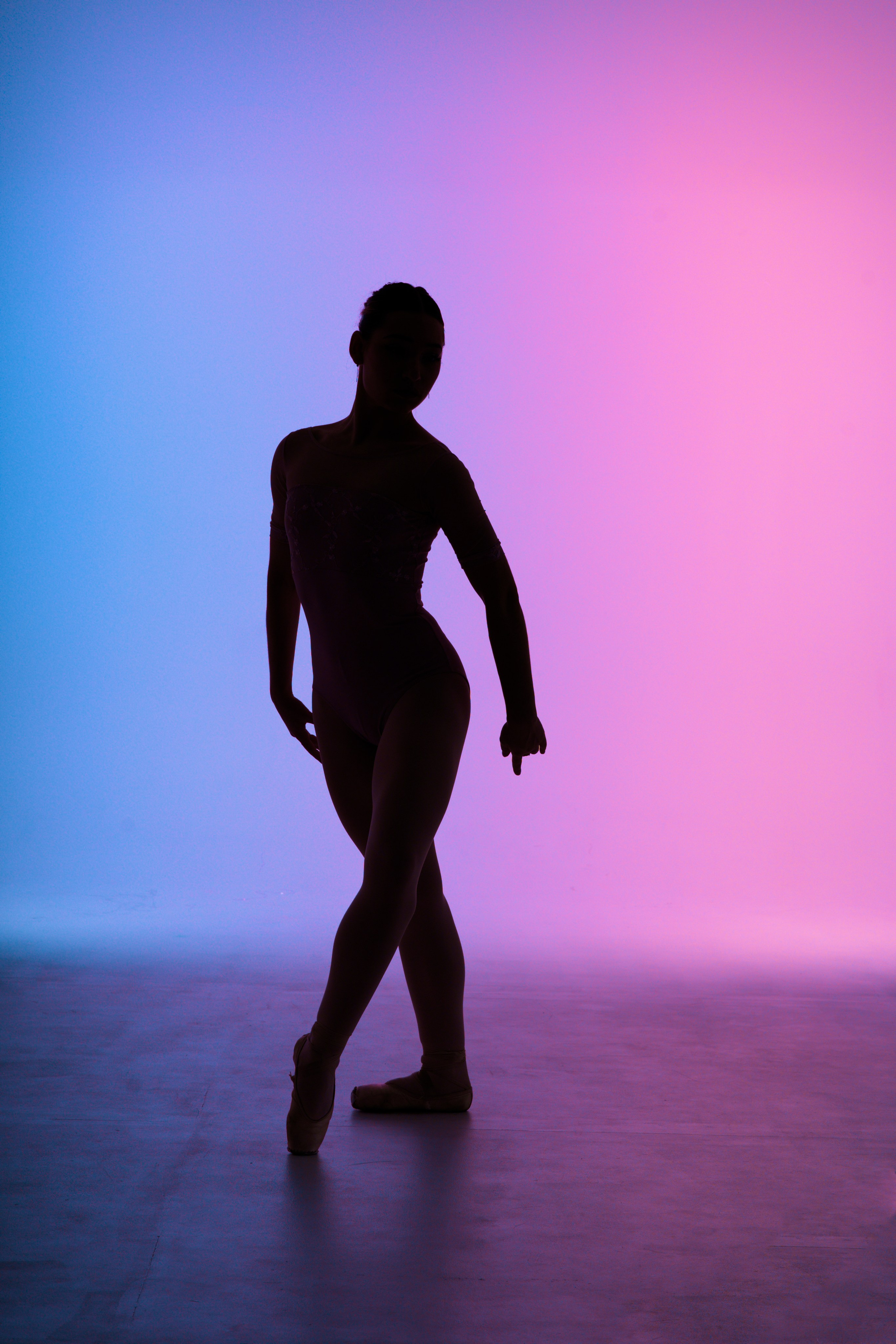 Спортивный фотограф в Тюмени: художественная съемка балета в стиле спорт-арт. Эстетичный силуэт балерины в классической позиции на фоне сине-розового неонового градиента. 