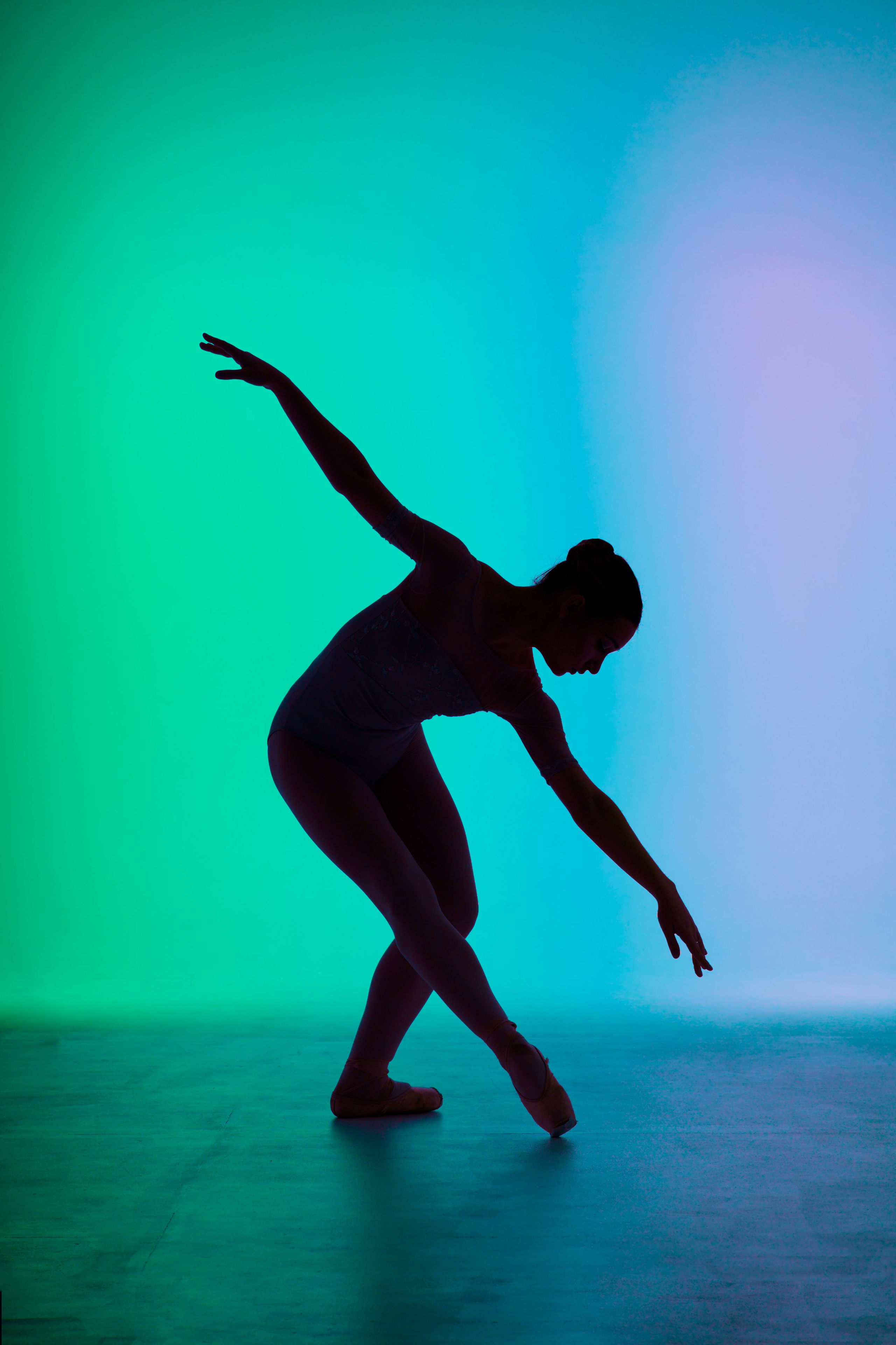 Графичный силуэт балерины в глубоком наклоне на фоне холодного градиентного света. Профессиональное портфолио в жанре спорт-арт, эстетика линий и формы.
