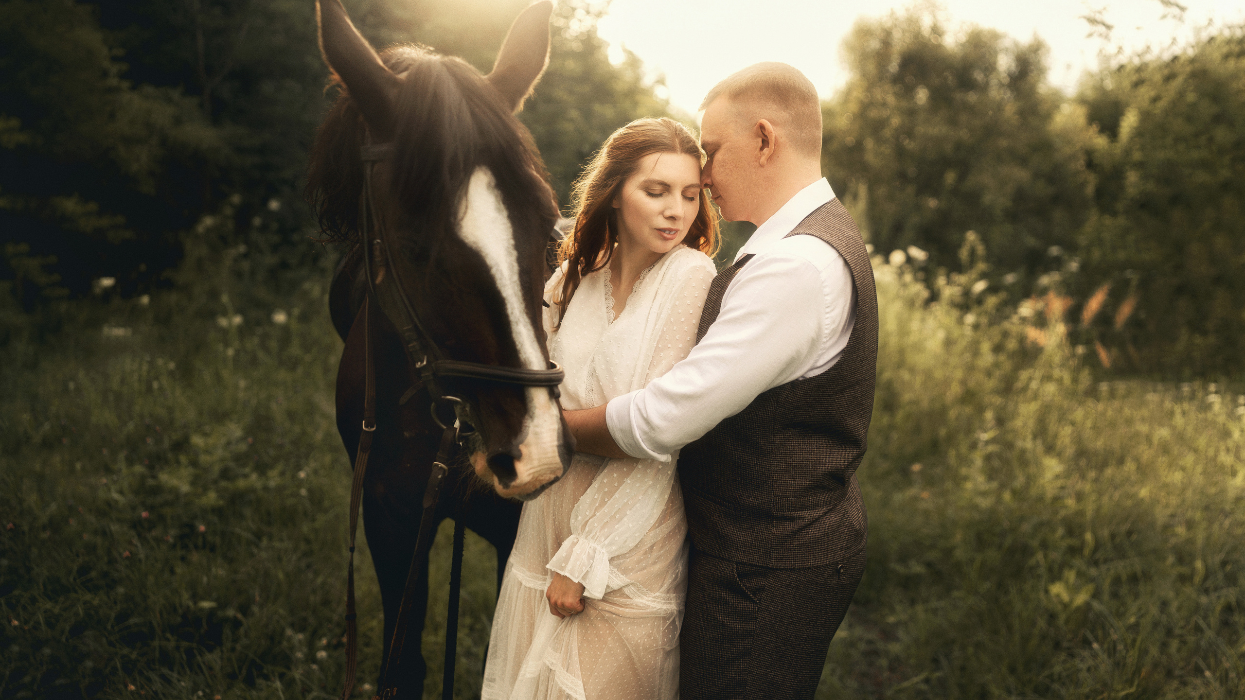 Красивая пара молодоженов стоит рядом с лошадью и обнимаются.