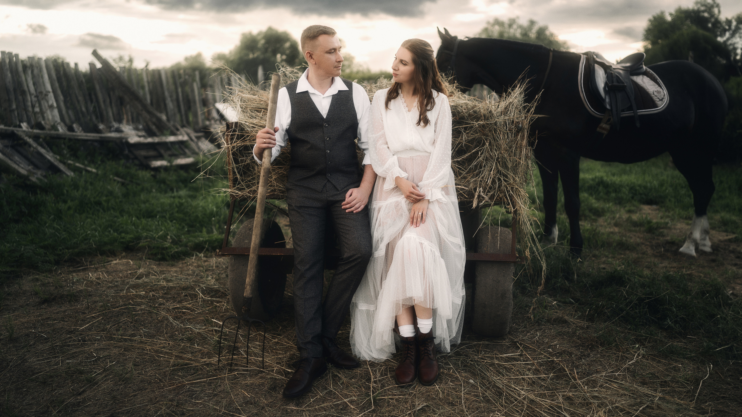 Жених и невеста сидят у сена и мило смотрят друг на друга. Фотограф Рома Янко.