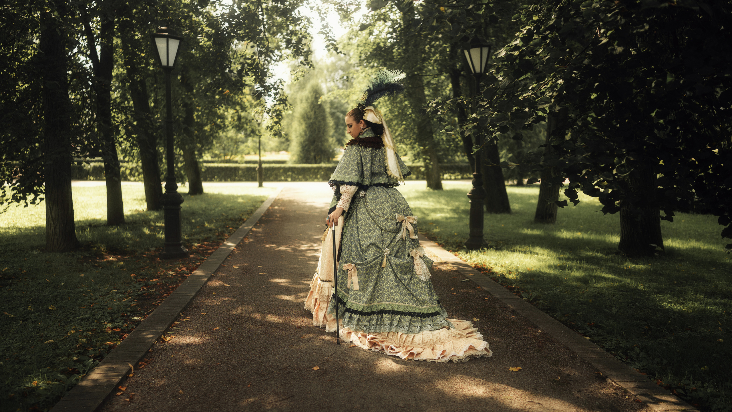 Девушка в шикарном, историческом платье прогуливается по парку.