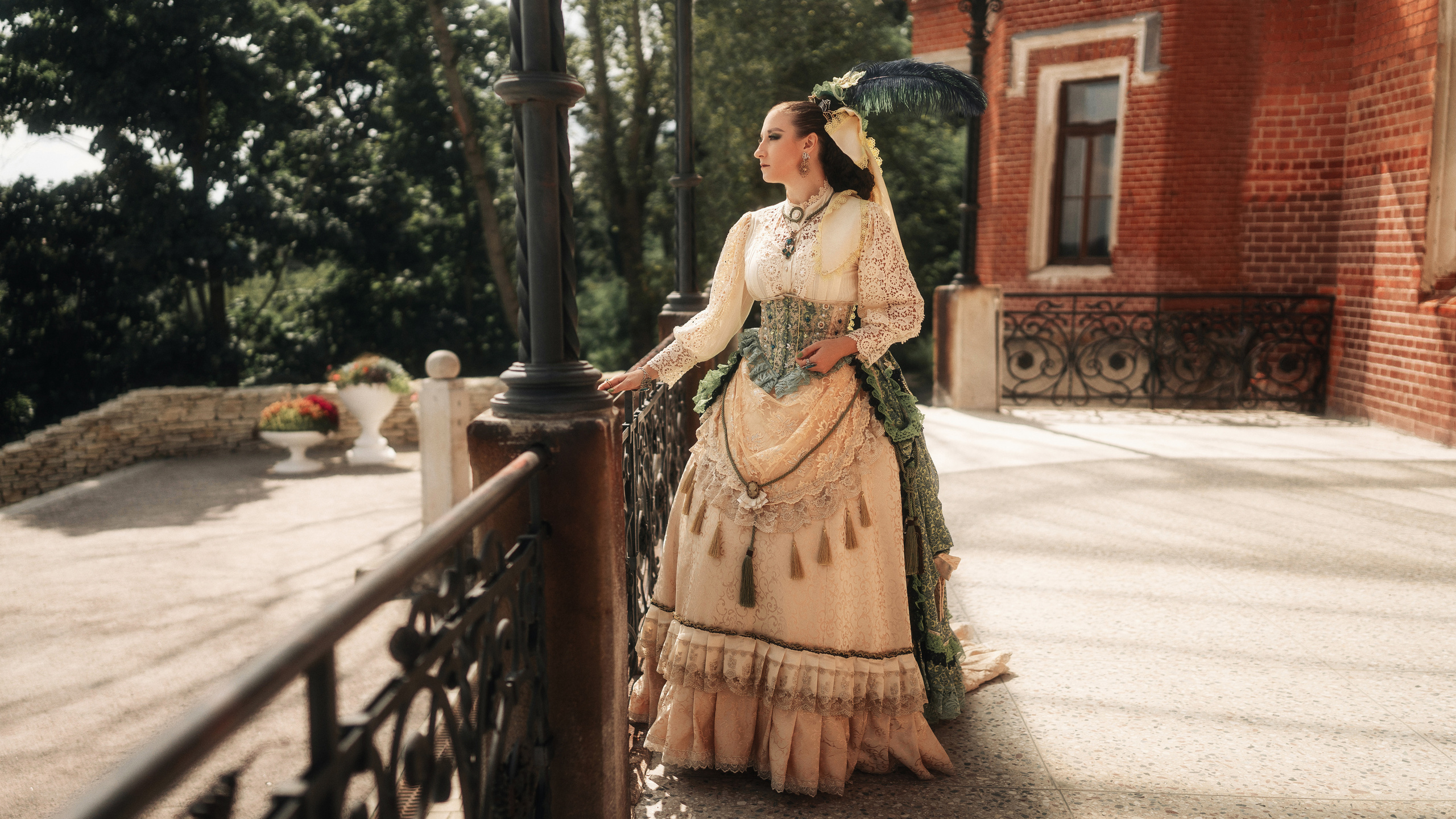 Девушка в шикарном, историческом платье смотрит в даль стоя на веранде.