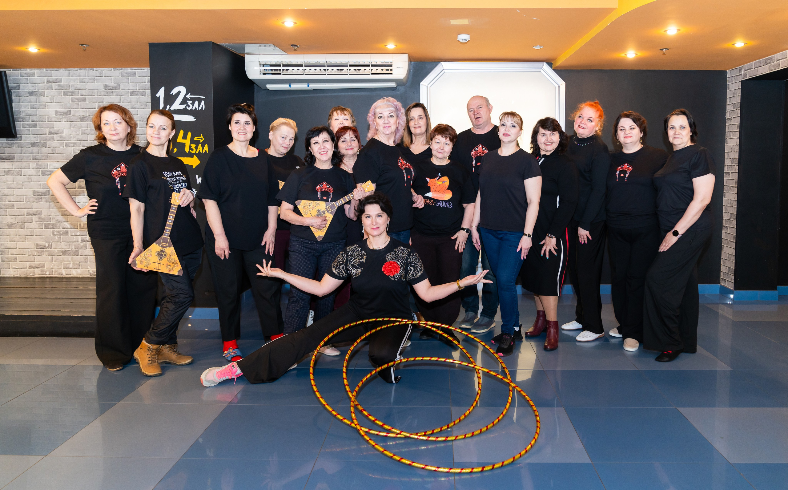 Групповое фото участников XII Международного фольклорного фестиваля «Сохраняем традиции» Санкт-Петербург 2026. Женщины в чёрных футболках с балалайками и обручами. Фото: Мальцев Евгений, evrednix.ru.