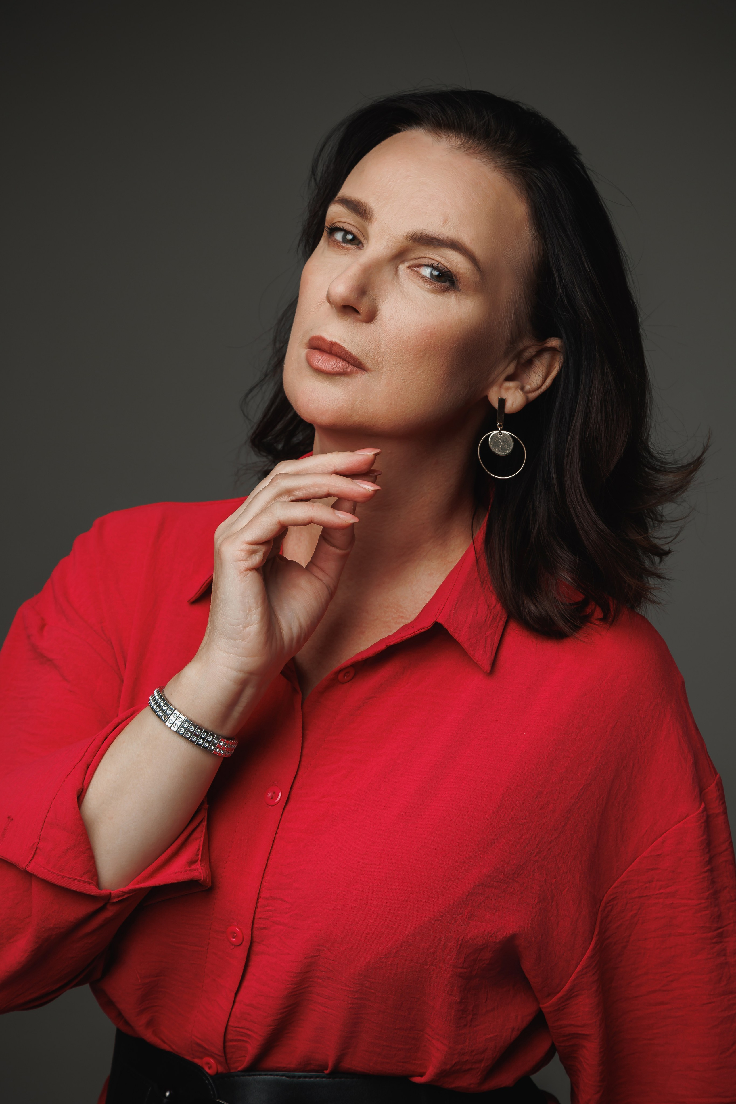 Яркий портрет психолога в красной рубашке на нейтральном сером фоне. Акцент на энергии и харизме.