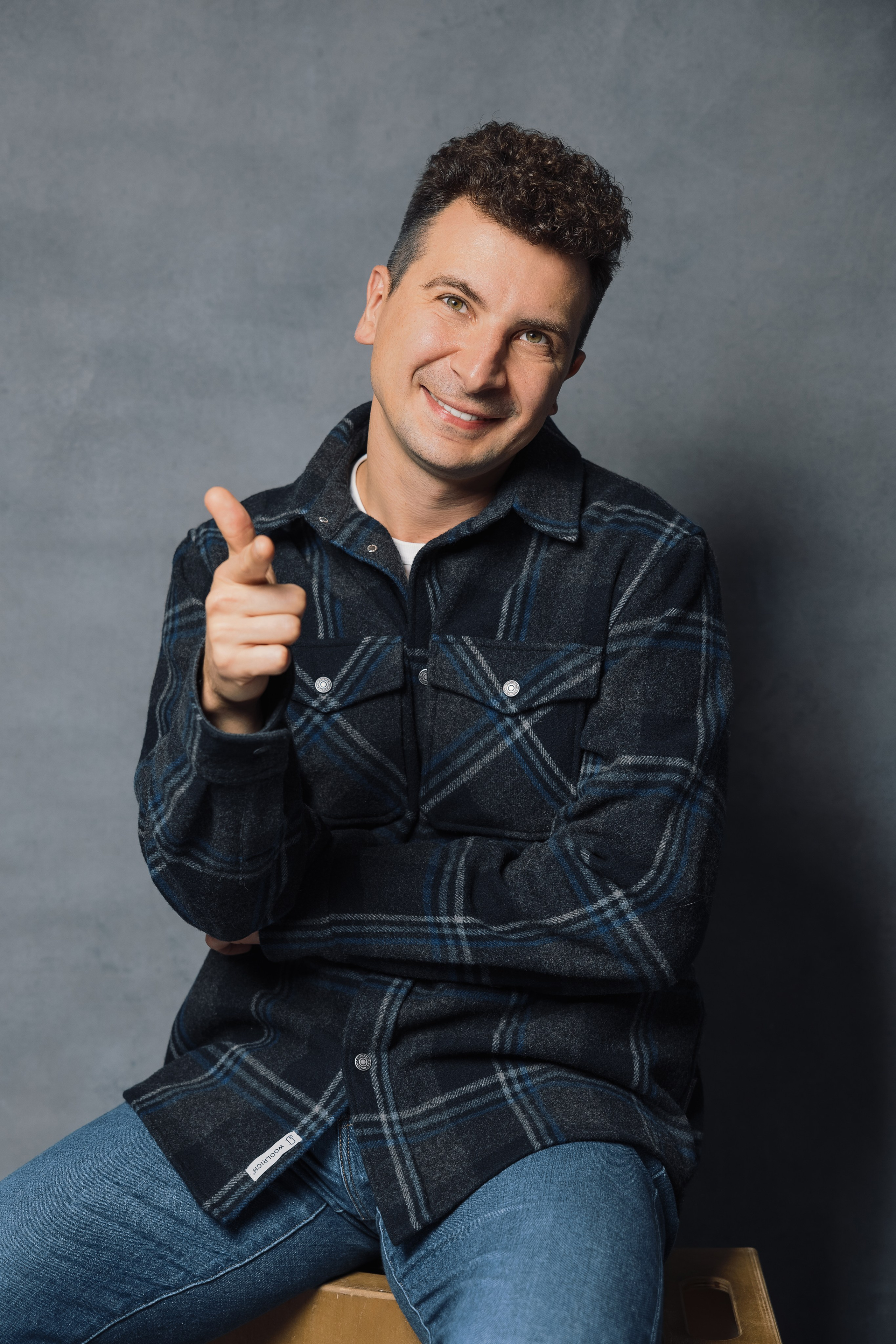 Портретная фотография мужчины в джинсах и клетчатой рубашке на сером фоне