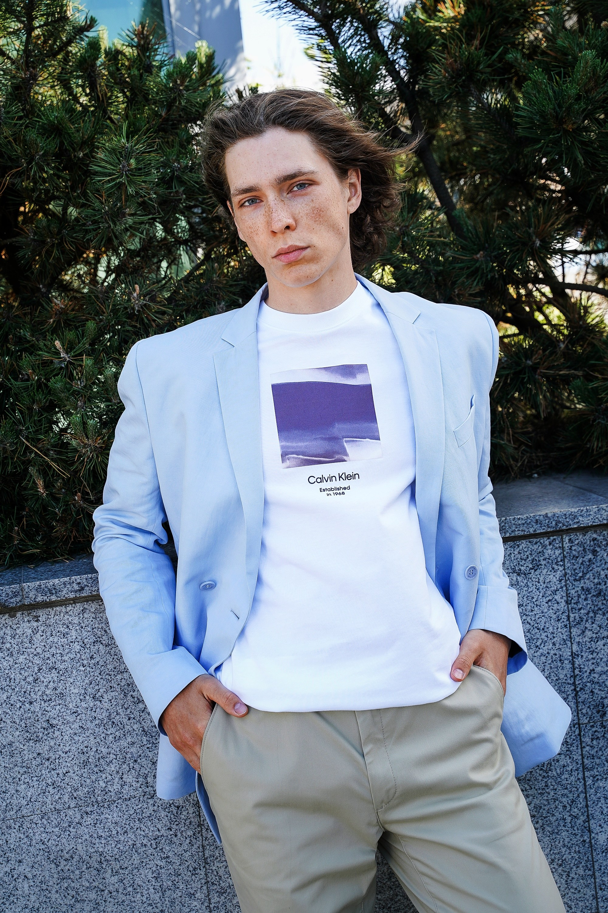 Парень модель с веснушками стоит на улице в голубом пиджаке и белой футболке