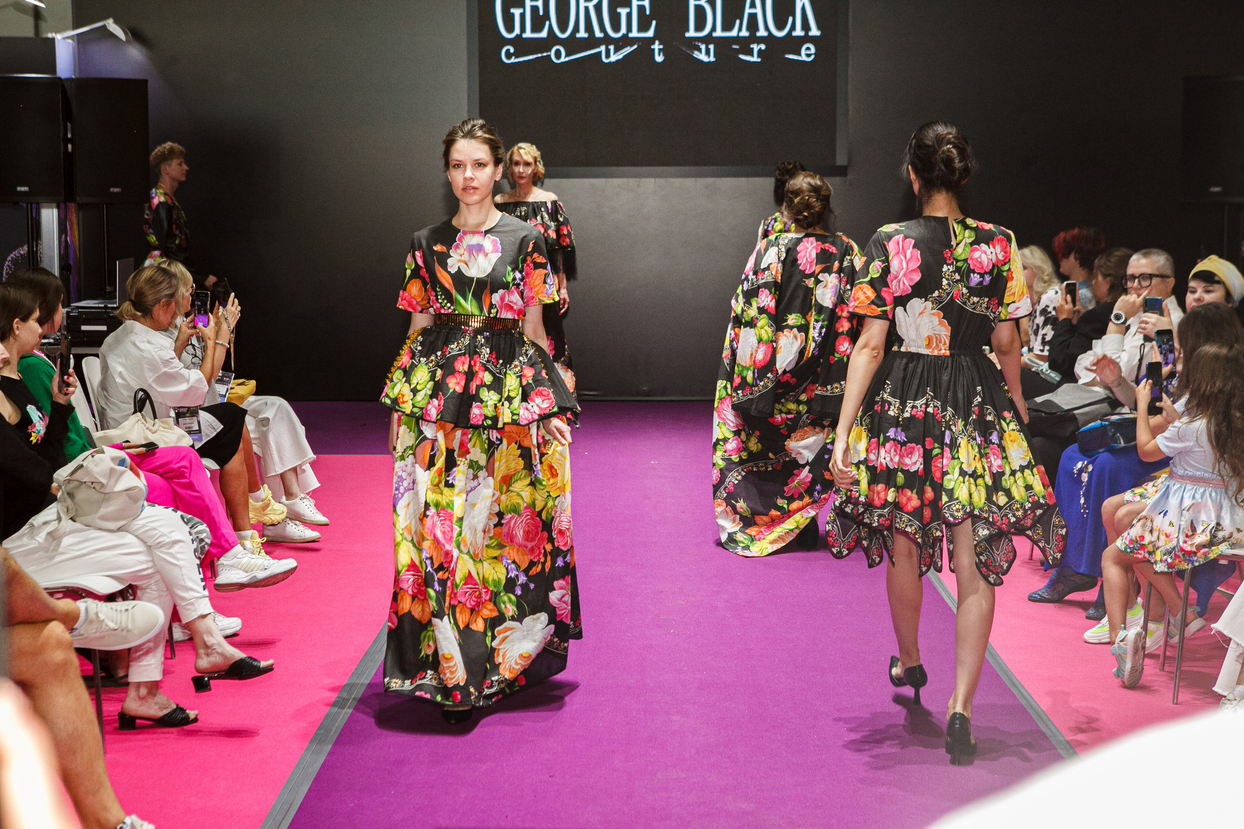  "Модели в ярких нарядах проходят по подиуму во время показа мод, освещенные яркими софитами и окруженные восторженными зрителями."