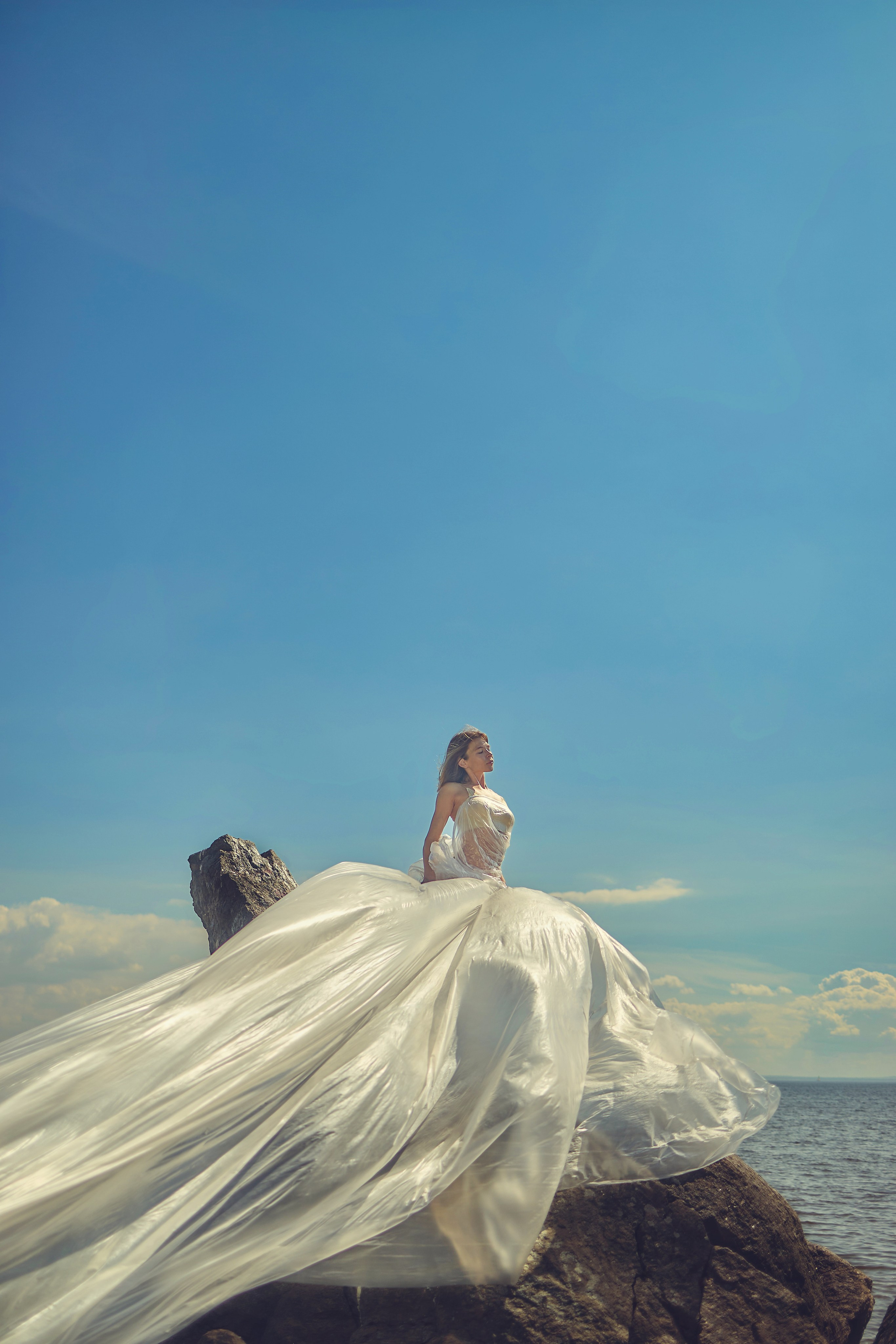 Уличная фотосесия девушка в парящем платье на камне, на берегу моря
