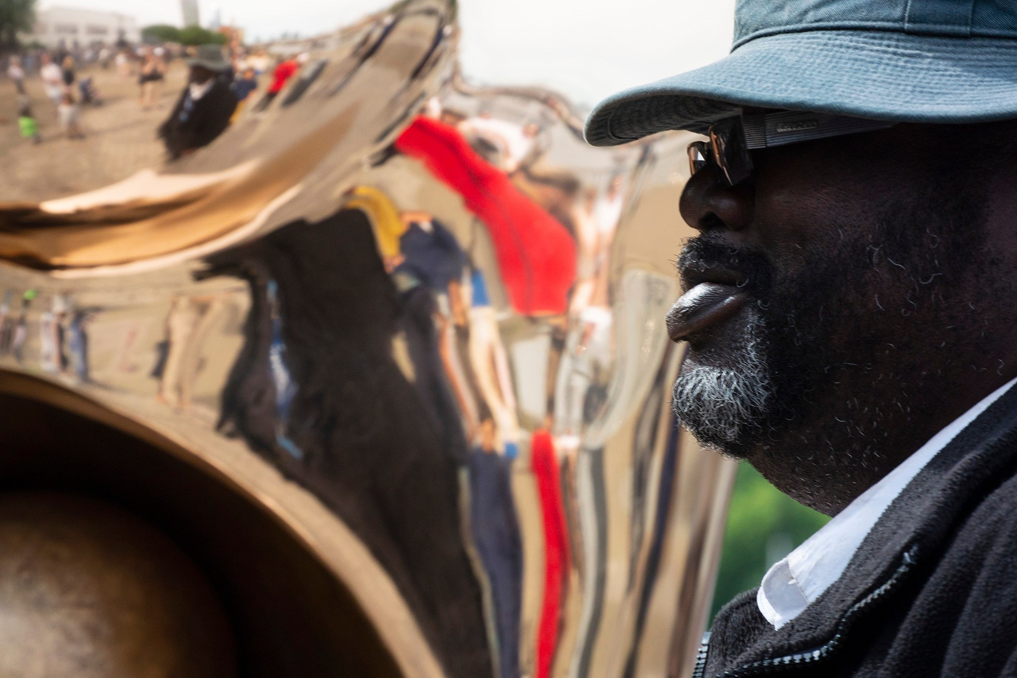 Крупный план мужчины в шляпе и солнцезащитных очках, стоящего рядом с абстрактной, высокоотражающей металлической скульптурой в Лондоне.