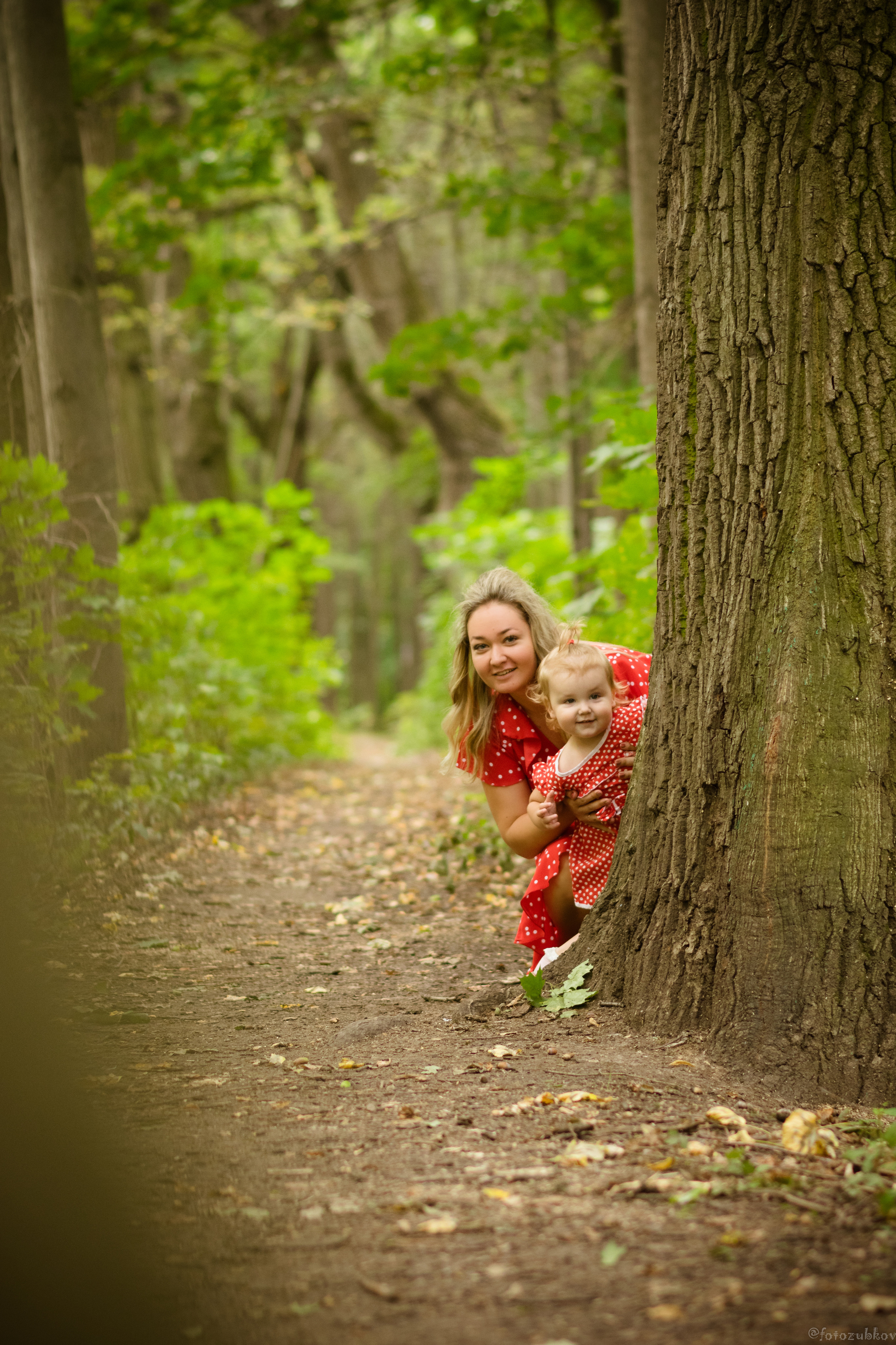 Мама с дочкой спрятались за деревом в лесу