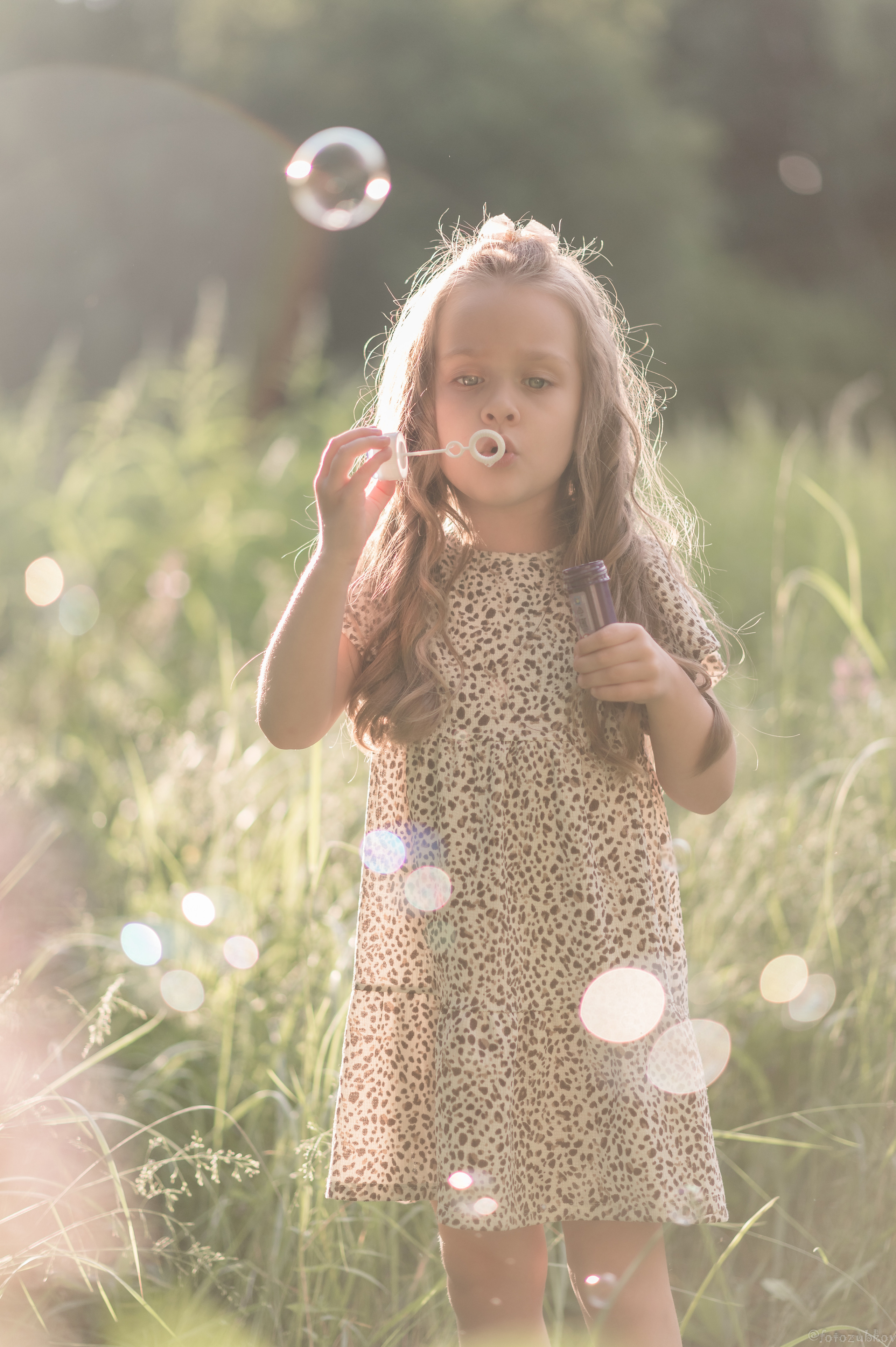 Маленькая девочка пускает мыльные пузыри в летнем парке