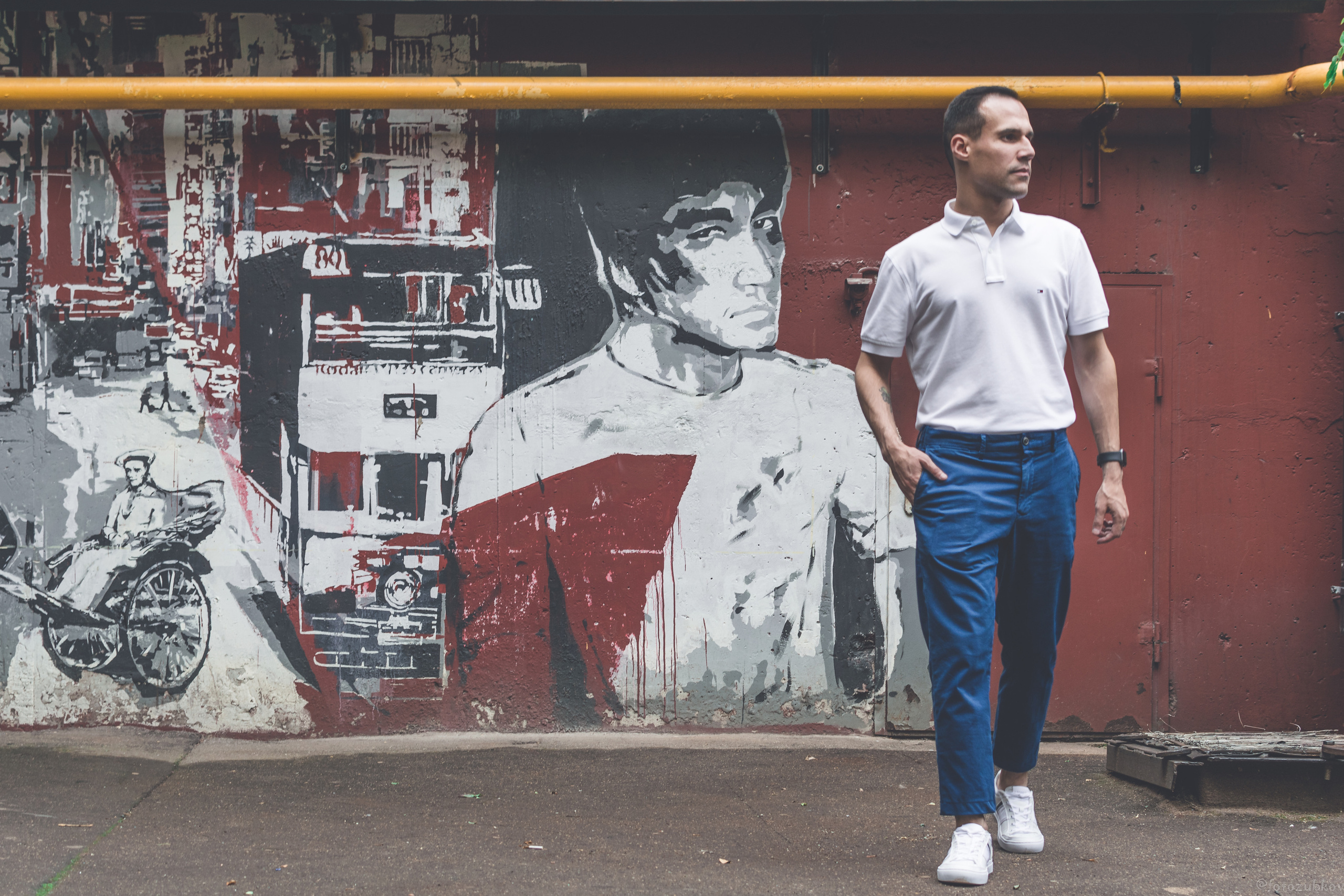 Молодой человек в поло напротив стены с изображением брюса ли