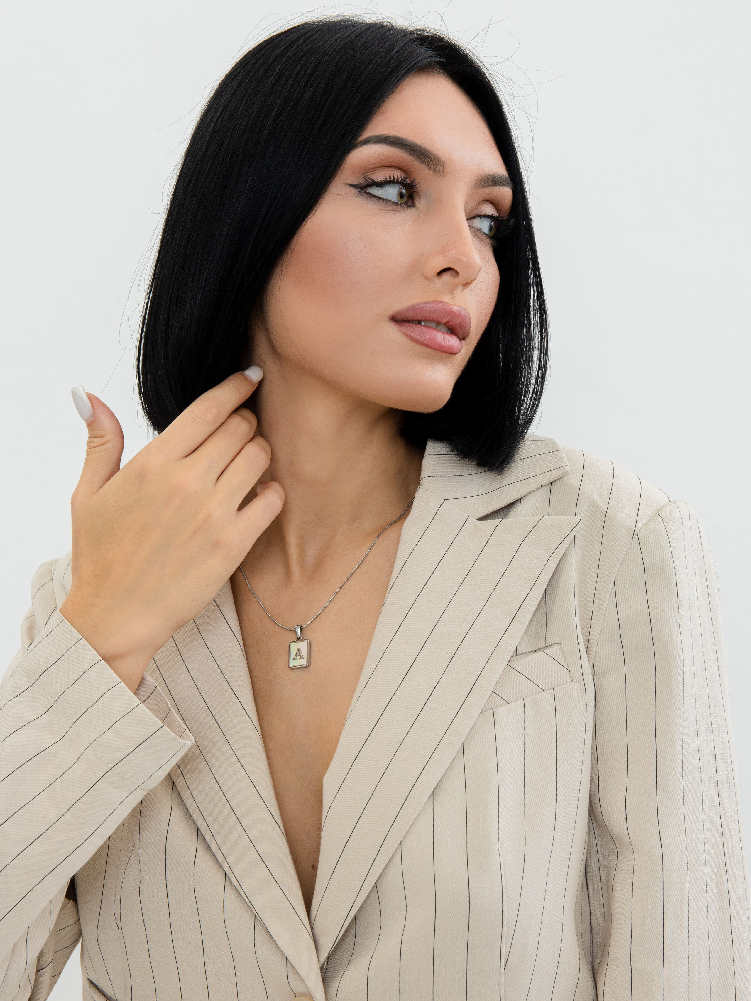 Портрет девушки брюнетки с зелеными глазами в молочном пиджаке и серебряным украшением на шее на белом фоне