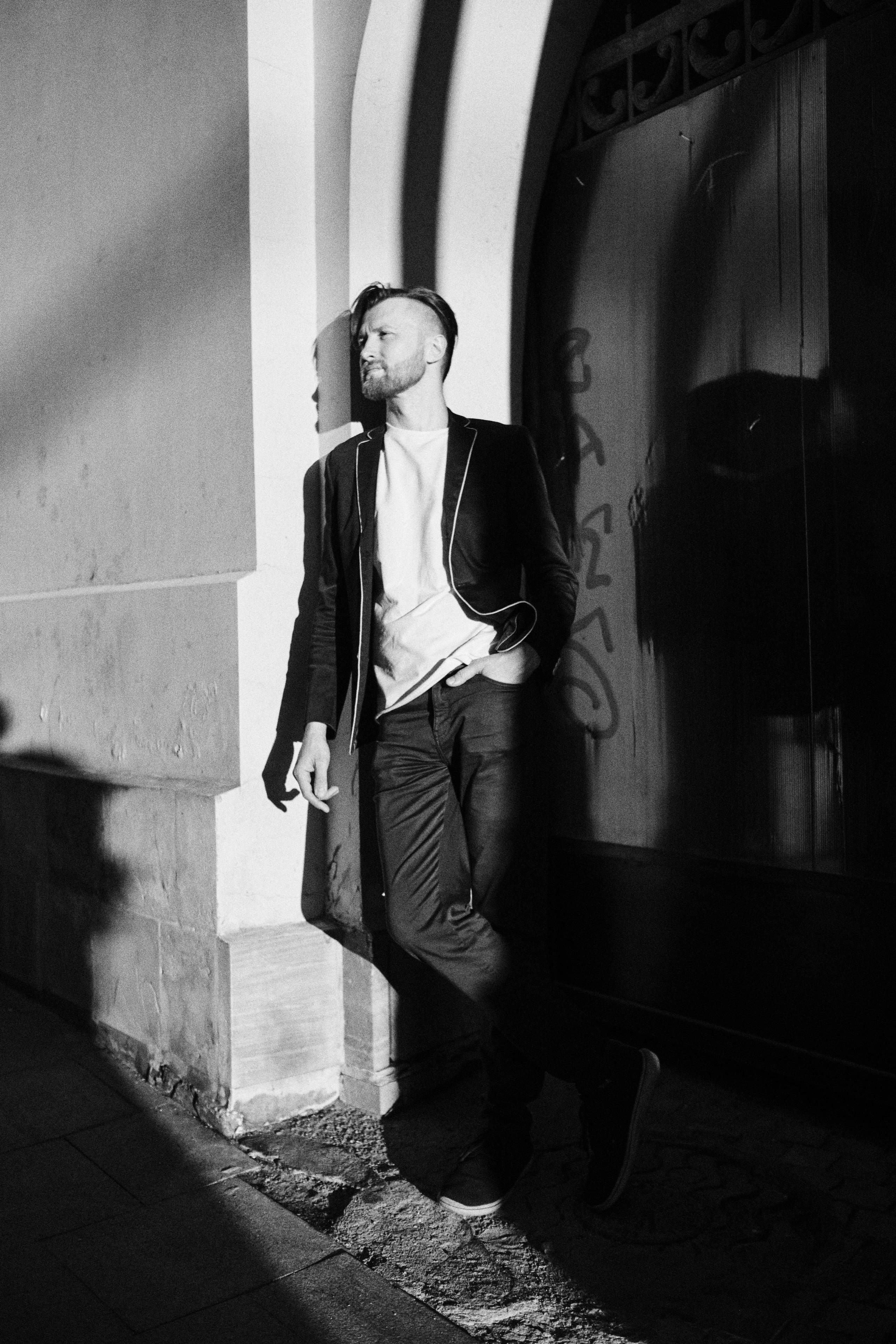 Мужчина в закатном солнце стоит у стены, на стене тень