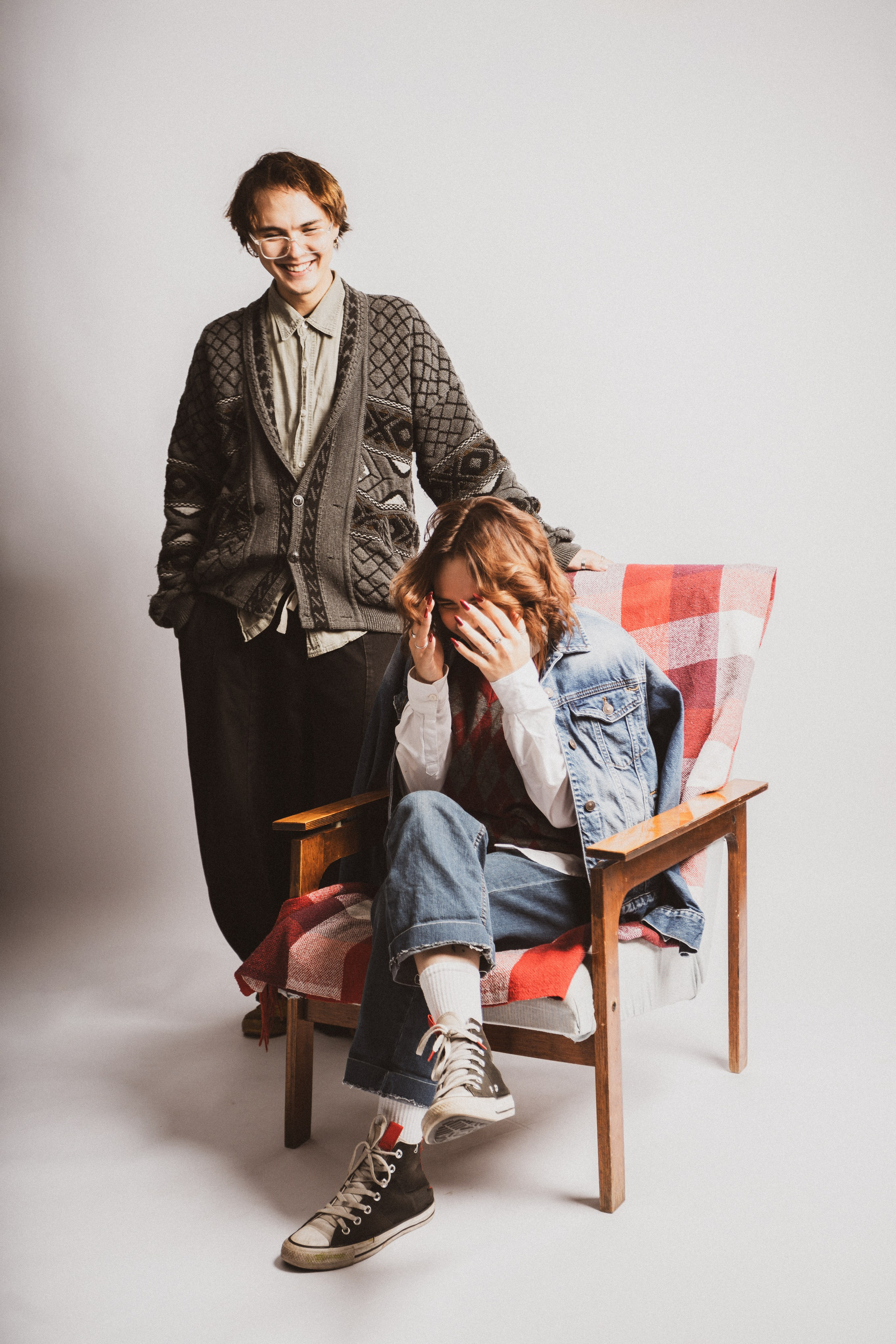 Девушка в черной куртке и джинсах сидит на стуле в студийном свете.