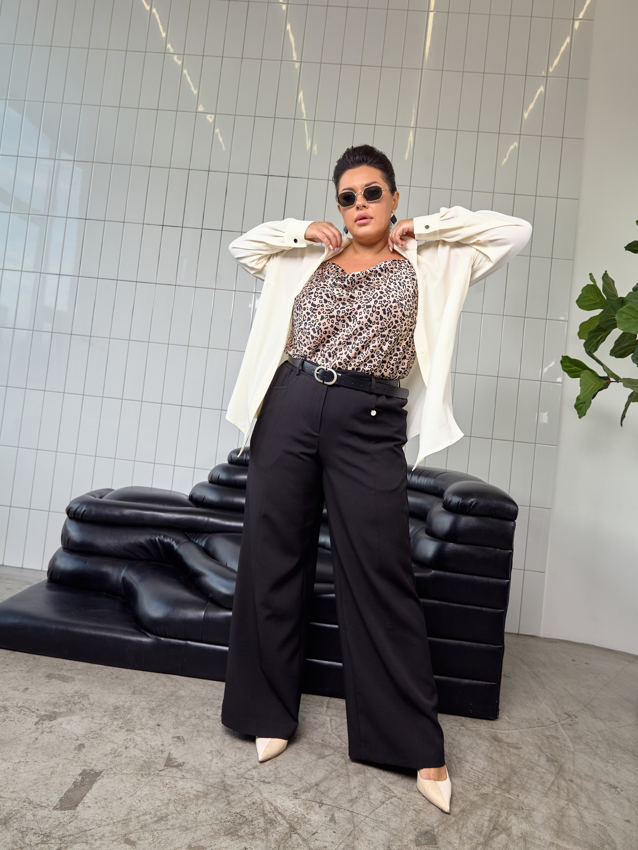 Элеонора Игнатова плюссайз модель в леопардовым топе, белой рубашке и черных брюках varra на фоне кафеля