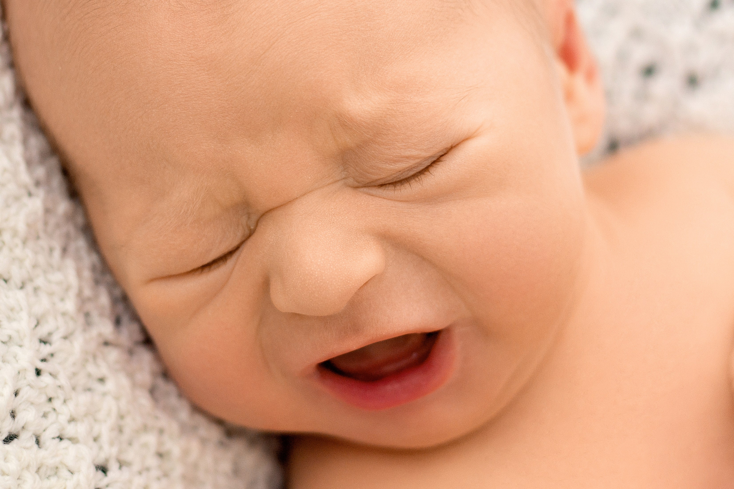 портрет плачущего новорожденного с закрытыми глазами и открытым беззубым ртом, лежащего на белом ажурном коврике 