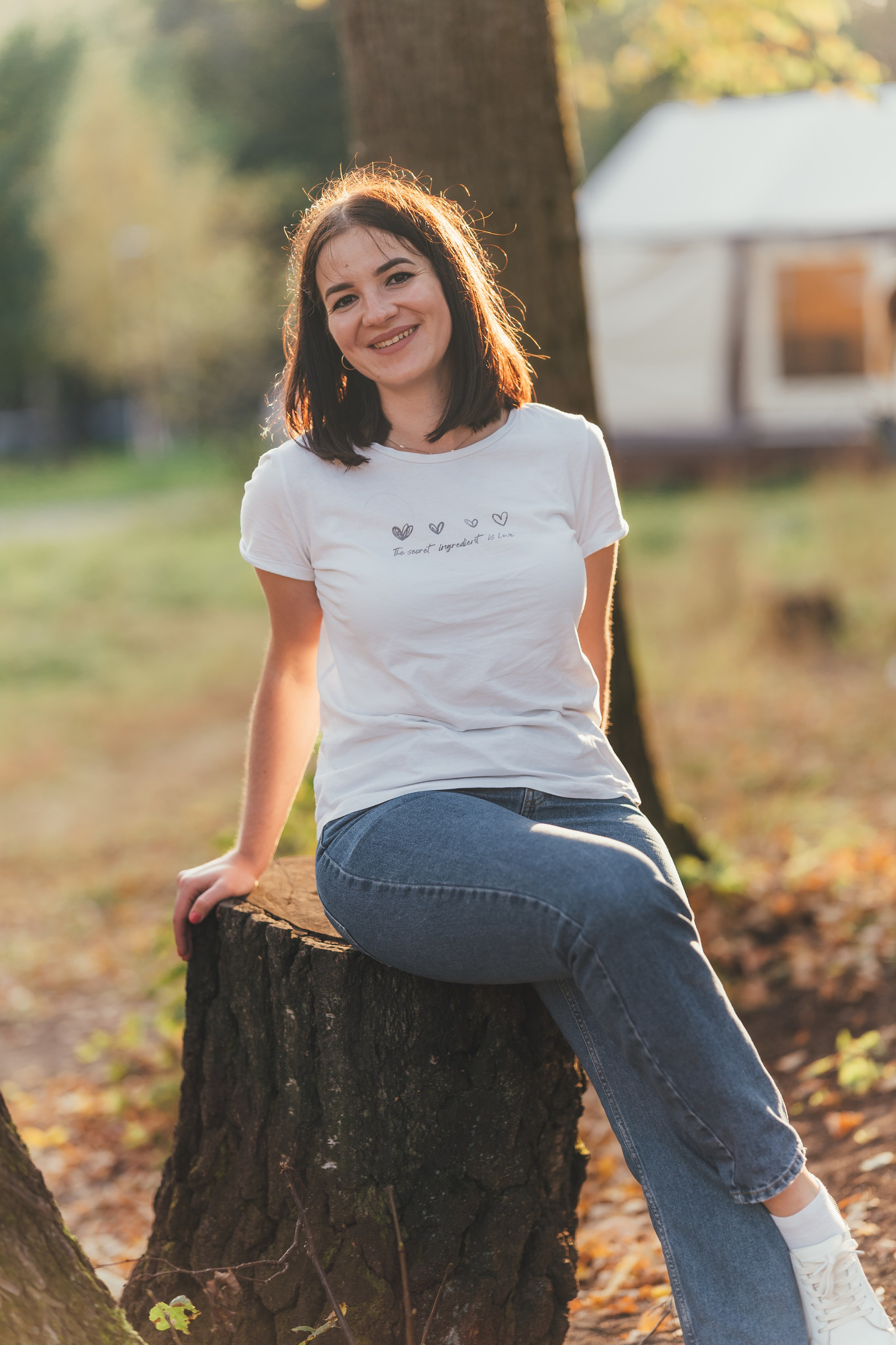 Молодая девушка позирует в лучах золотого солнца на пеньке в лесу