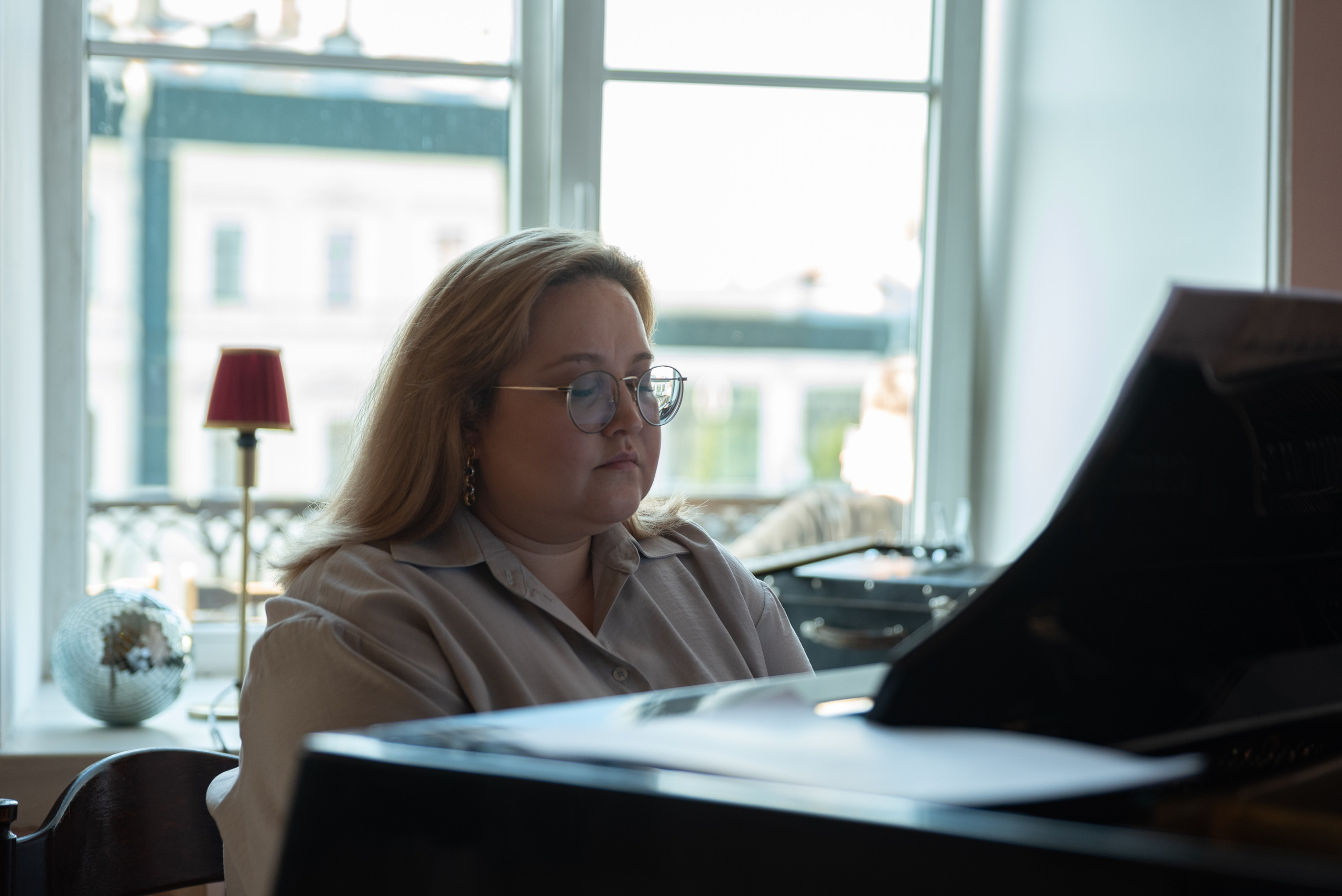 Женщина играет на рояле напротив окна