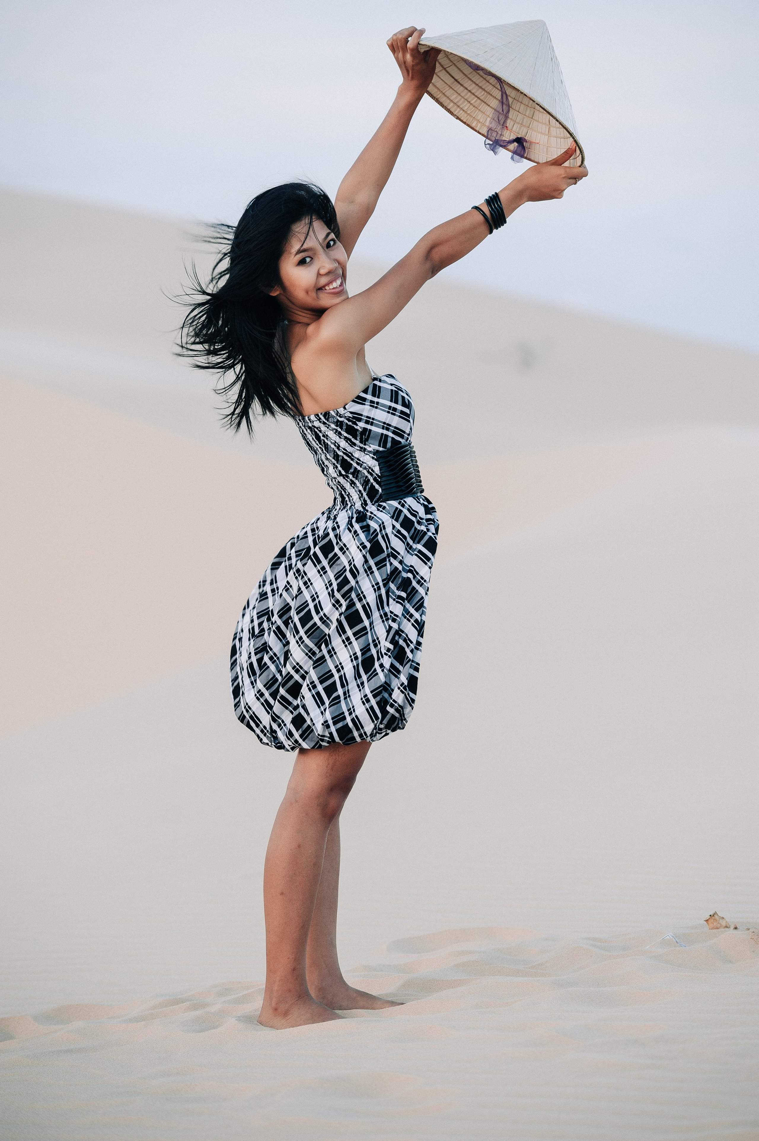 Молодая вьетнамская девушка в платье стоит подняв в руках вьетнамскую панаму в дюнах Муине, Вьетнам