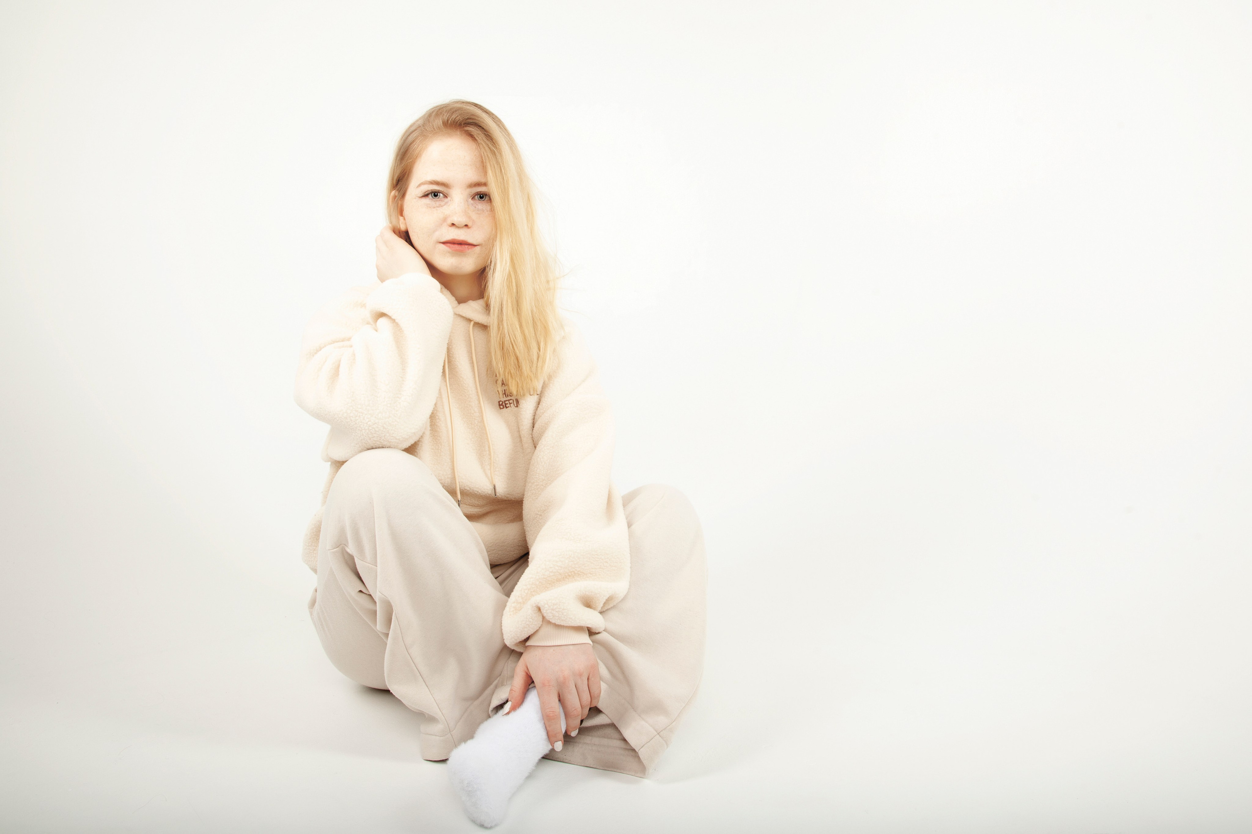 Портрет светловолосой и голубоглазой девушки с веснушками. В светлой одежде на белом фоне.