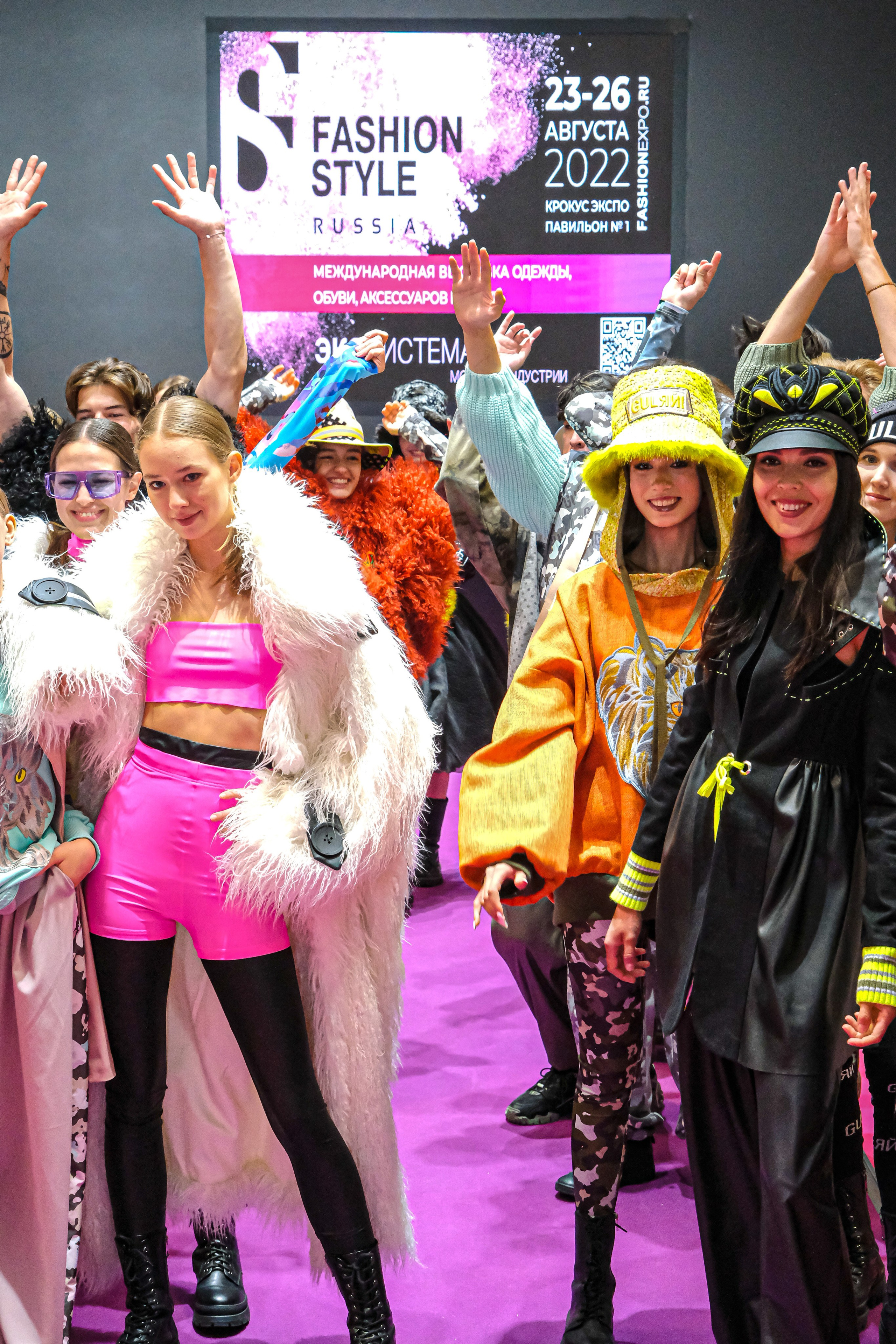  "Модели в ярких нарядах проходят по подиуму во время показа мод, освещенные яркими софитами и окруженные восторженными зрителями."